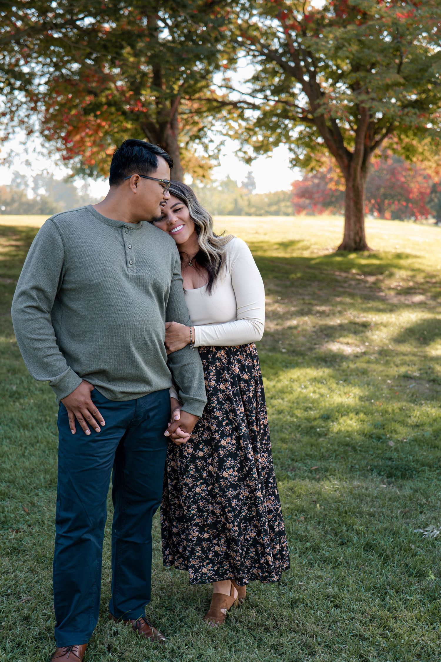 Couple embraces in a sunny autumn field with trees in the background during an outdoor photoshoot in Roseville, CA