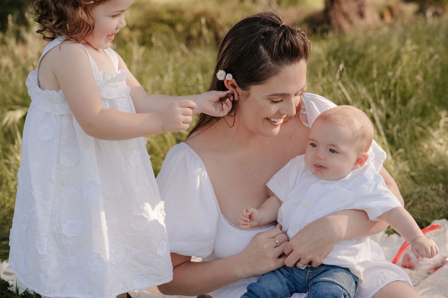 Tender family moment on a white blanket outdoors with a small baby.
