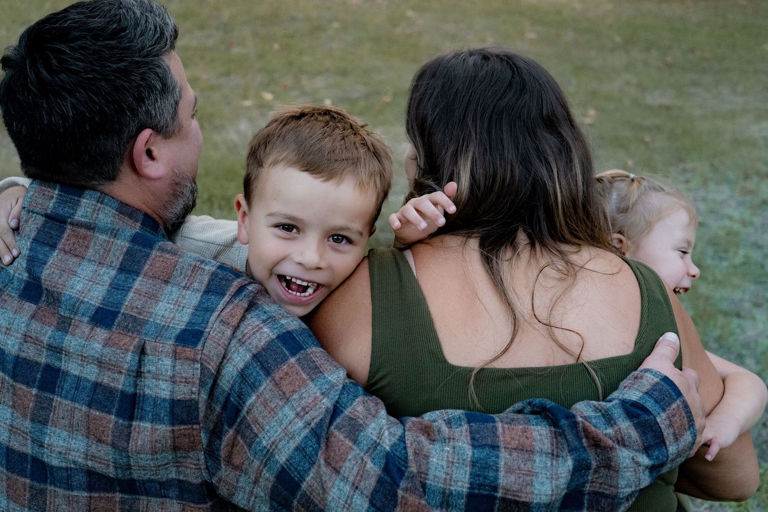 A group of people gather around a small pond or stream while wearing casual outdoor clothing and plaid shirts.