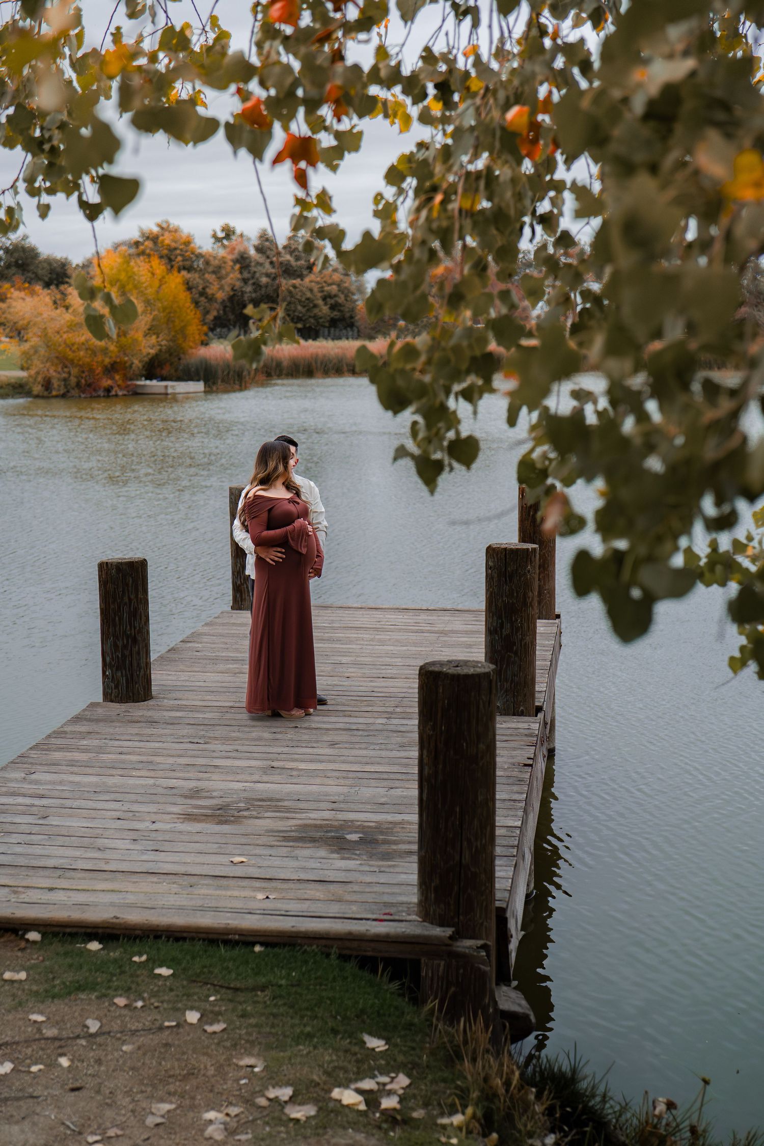 Scenic maternity photos on wooden dock surrounded by fall trees and lake views in Roseville, CA