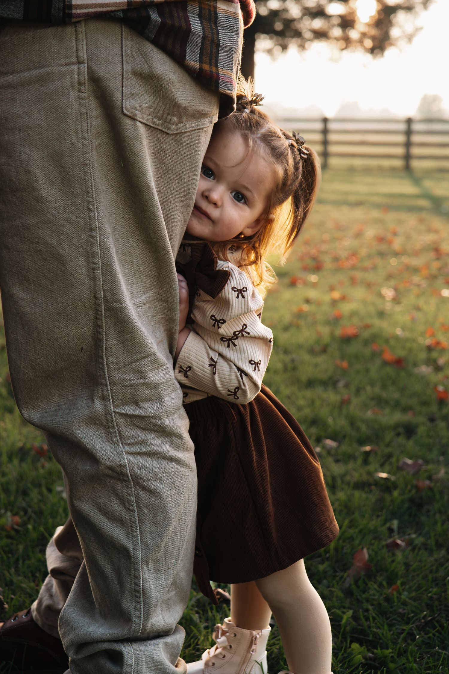 Playful child peeking around adult's legs in an autumn field in Roseville, CA