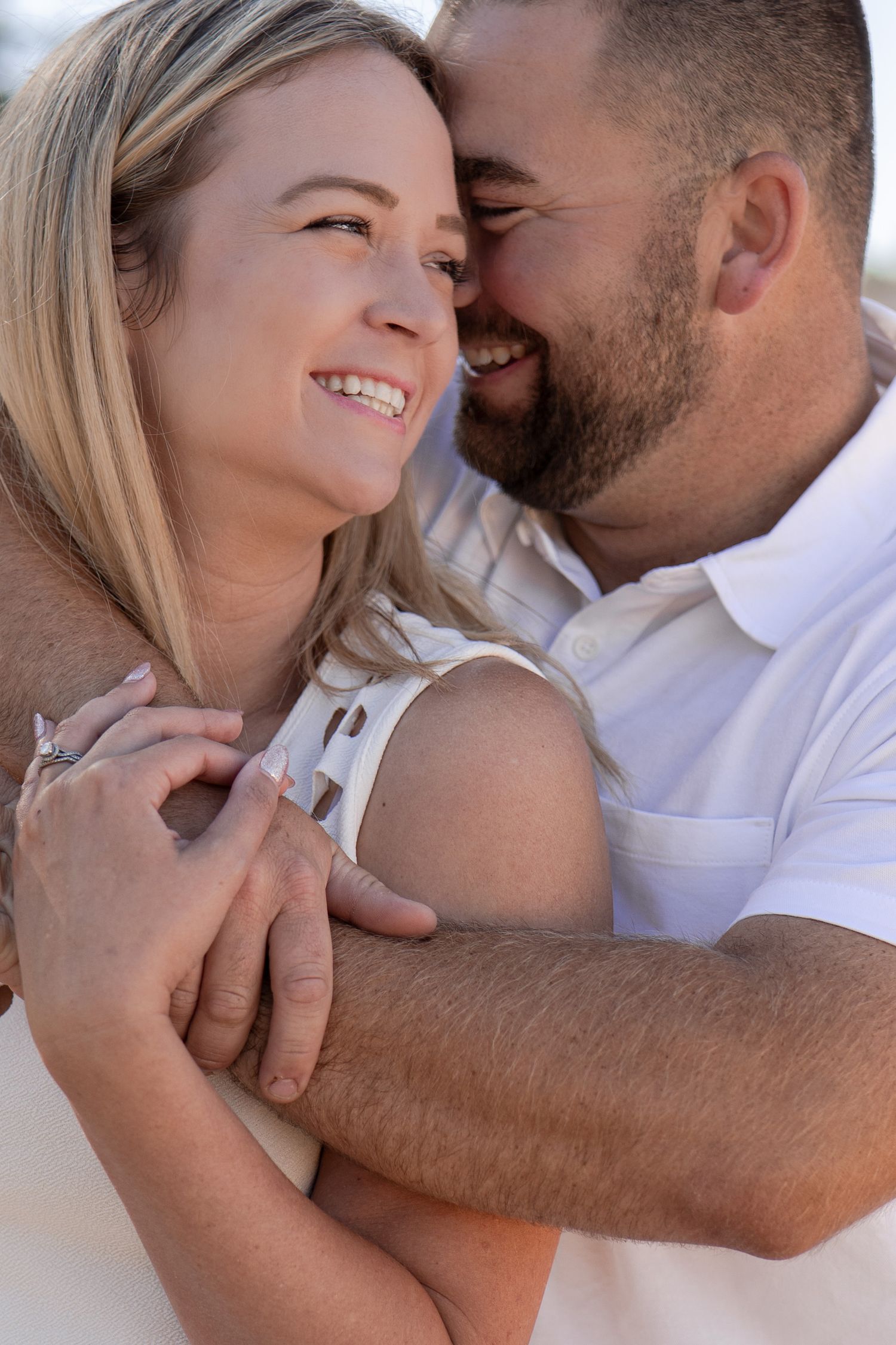 Romantic couple embracing in white outfits against natural outdoor backdrop.