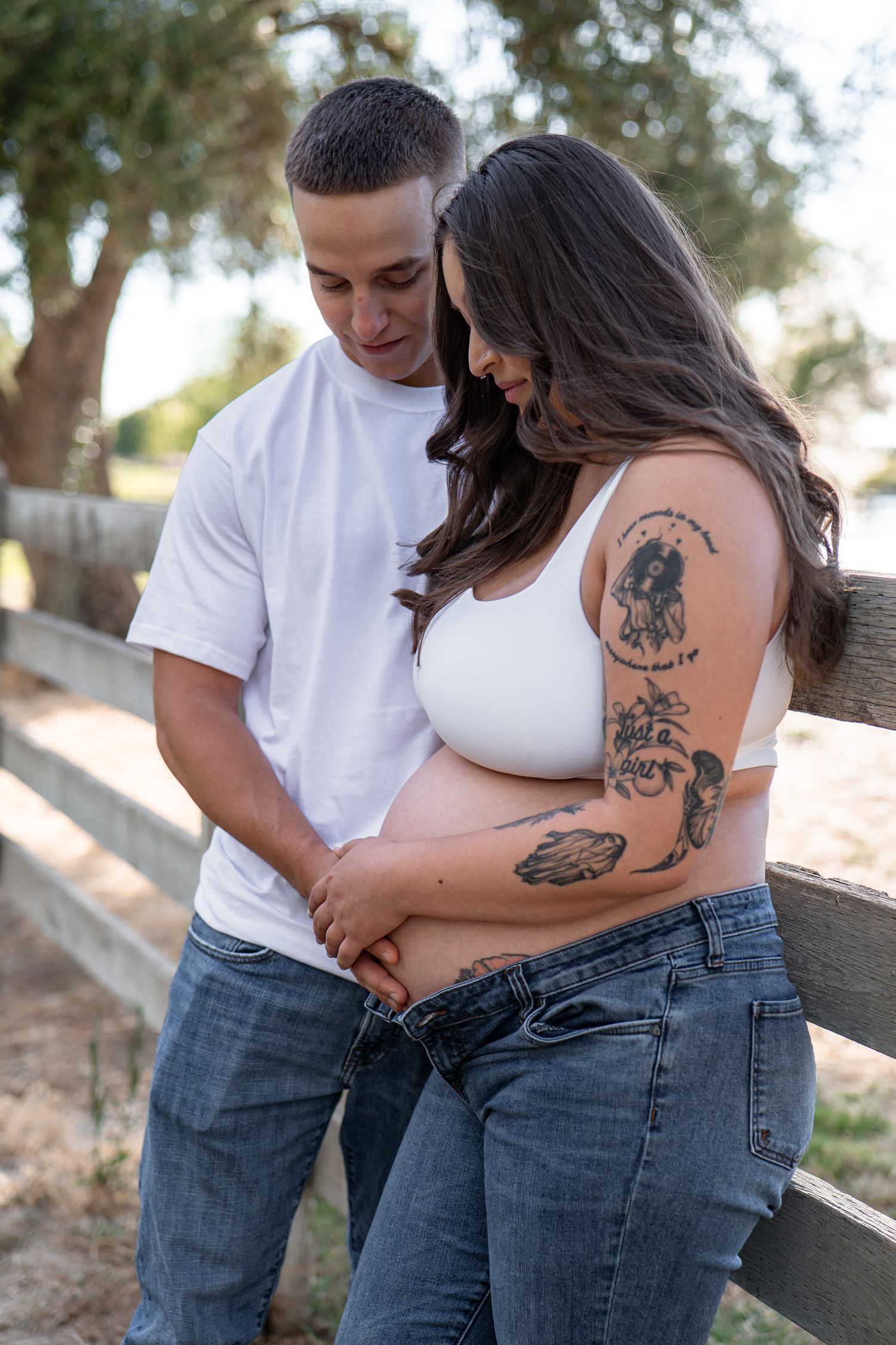 Outdoor maternity photography session showing artistic tattoos and casual attire.