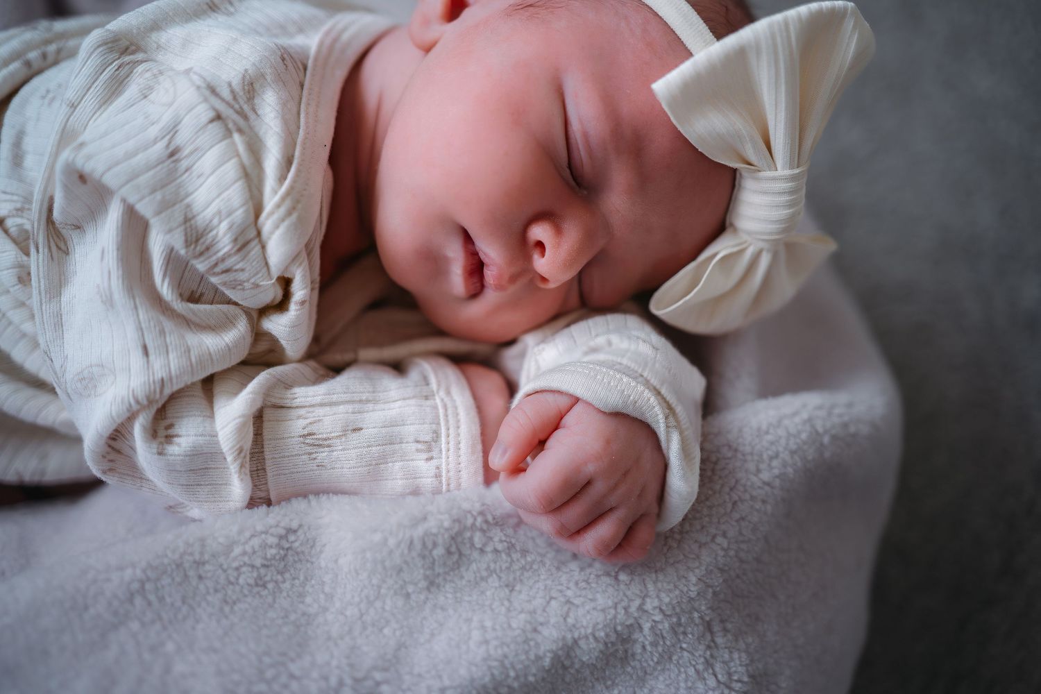 A sleeping baby in a white outfit rests peacefully on soft gray fabric in a series of connected photos.