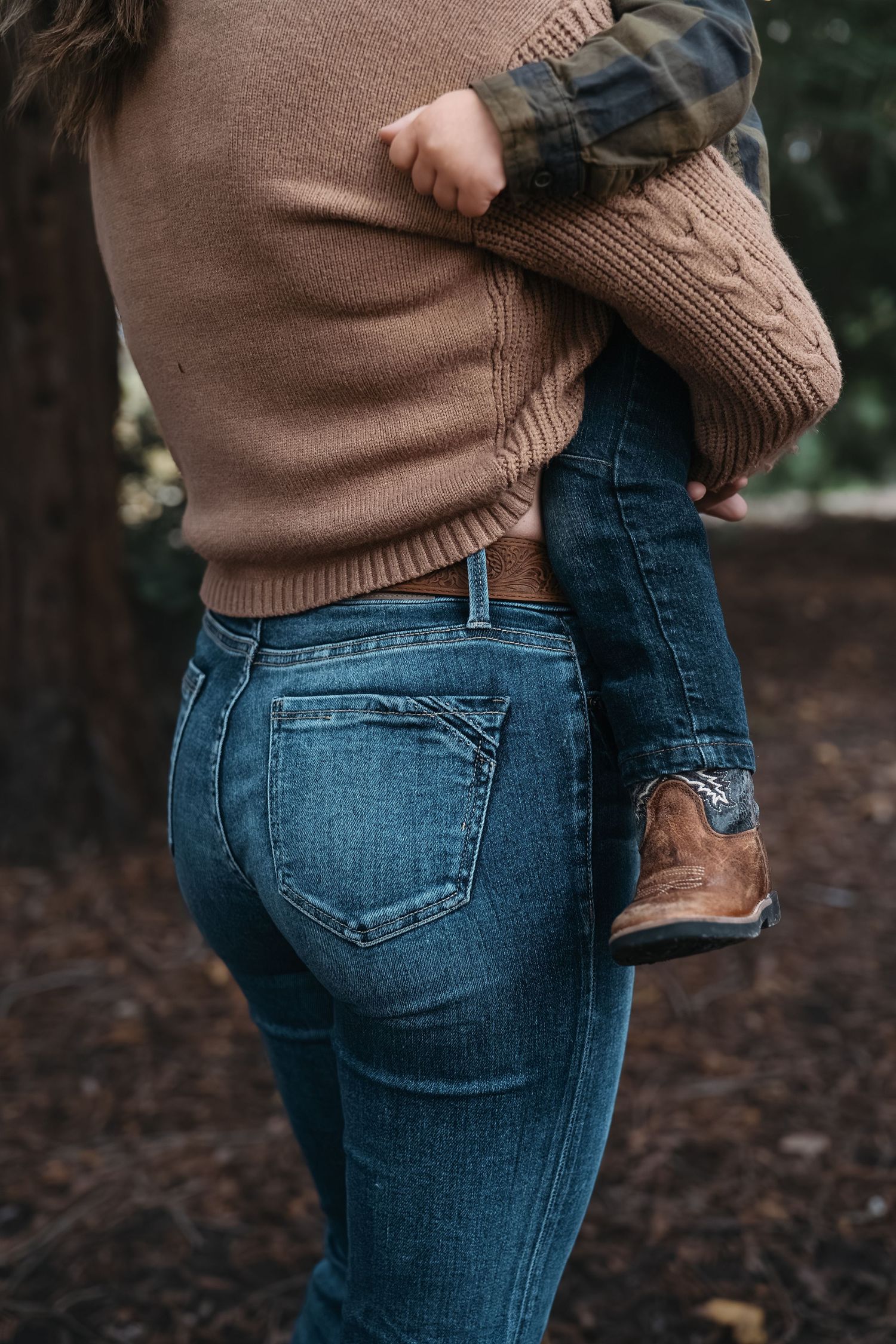 Close-up view of someone wearing a brown sweater holding a child in blue jeans outdoors in Roseville, CA