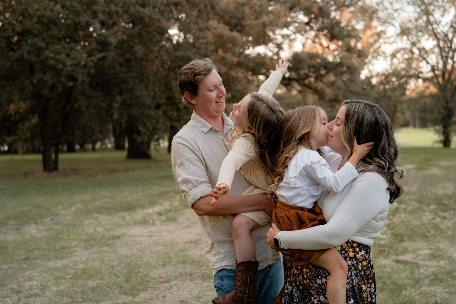 A family shares a tender moment together in a park at sunset with trees in the background.