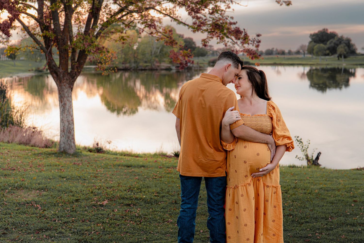 Couple in matching mustard yellow outfits embrace by a serene lake during sunset.