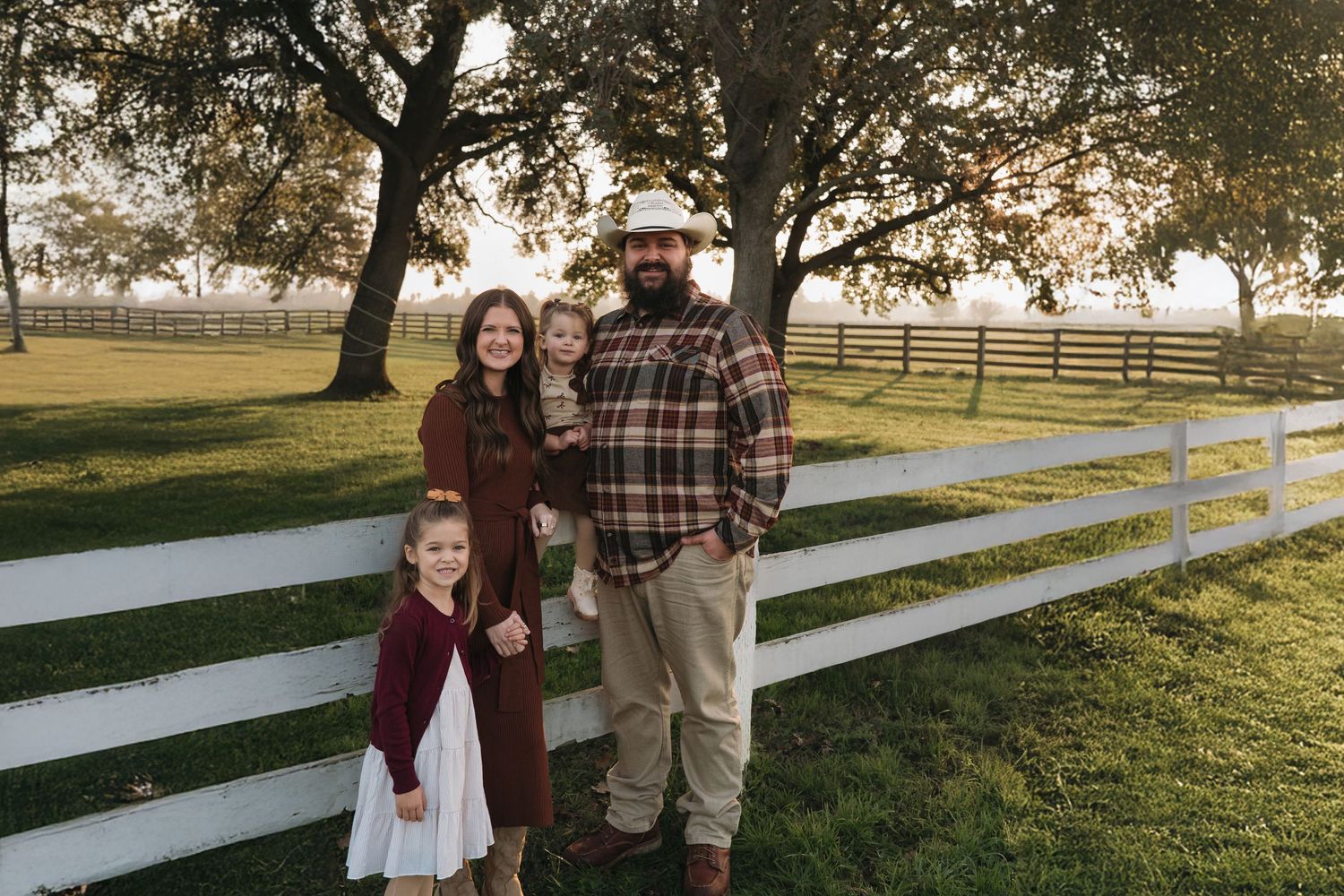 Family standing by white fence during golden hour in a pastoral setting in Roseville, CA