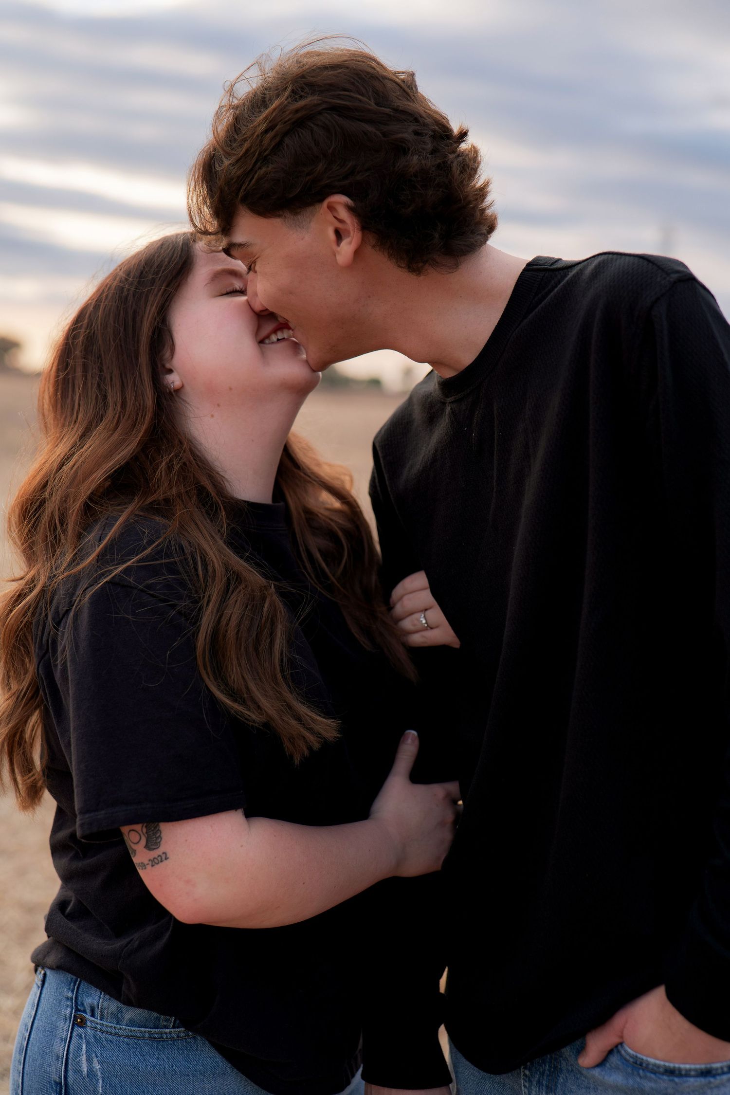 Romantic couple sharing intimate moments in black shirts against a cloudy sky background in Roseville, CA