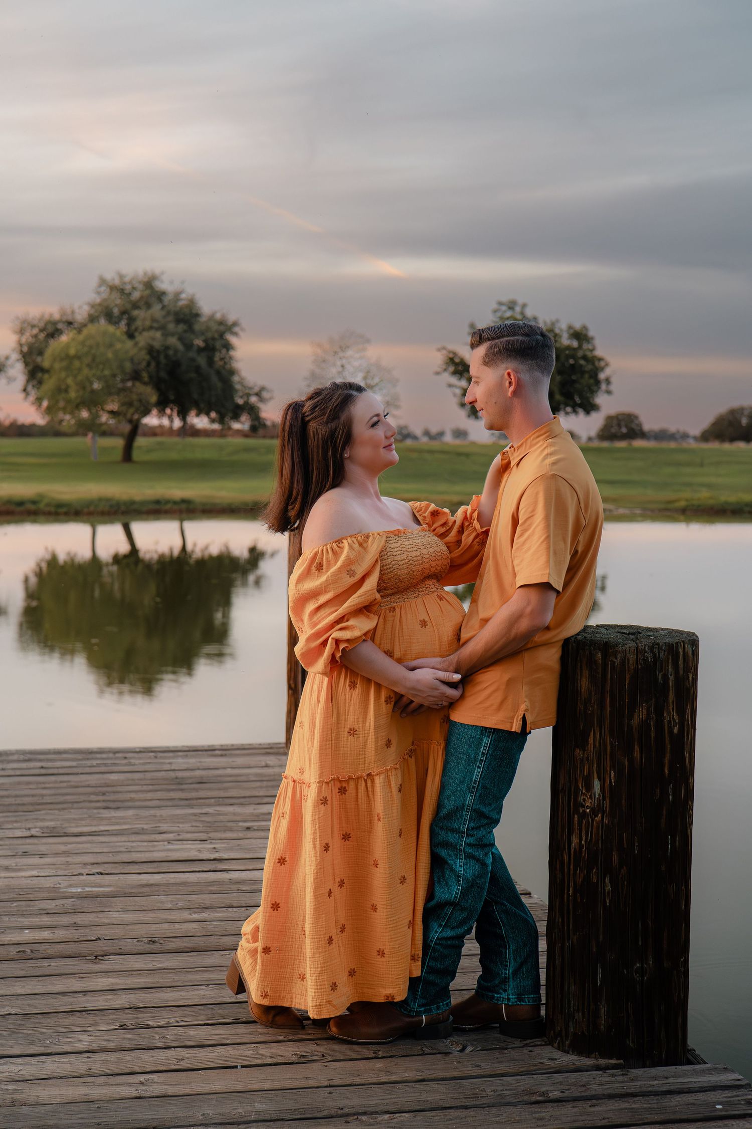 Couple stands on wooden dock by lake during sunset maternity photoshoot in Roseville, CA