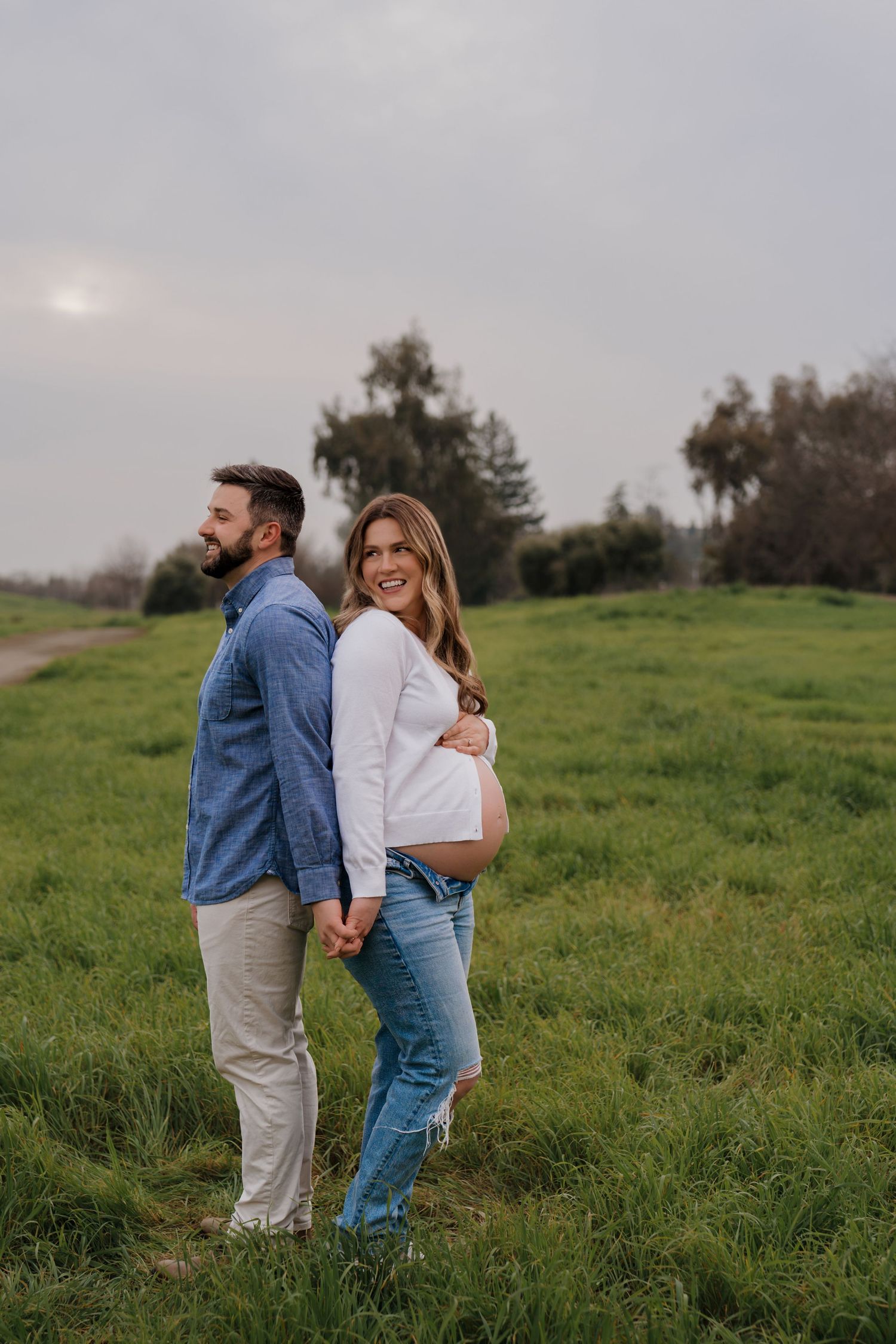 A couple embraces in a romantic moment while standing in a lush green meadow at dusk.