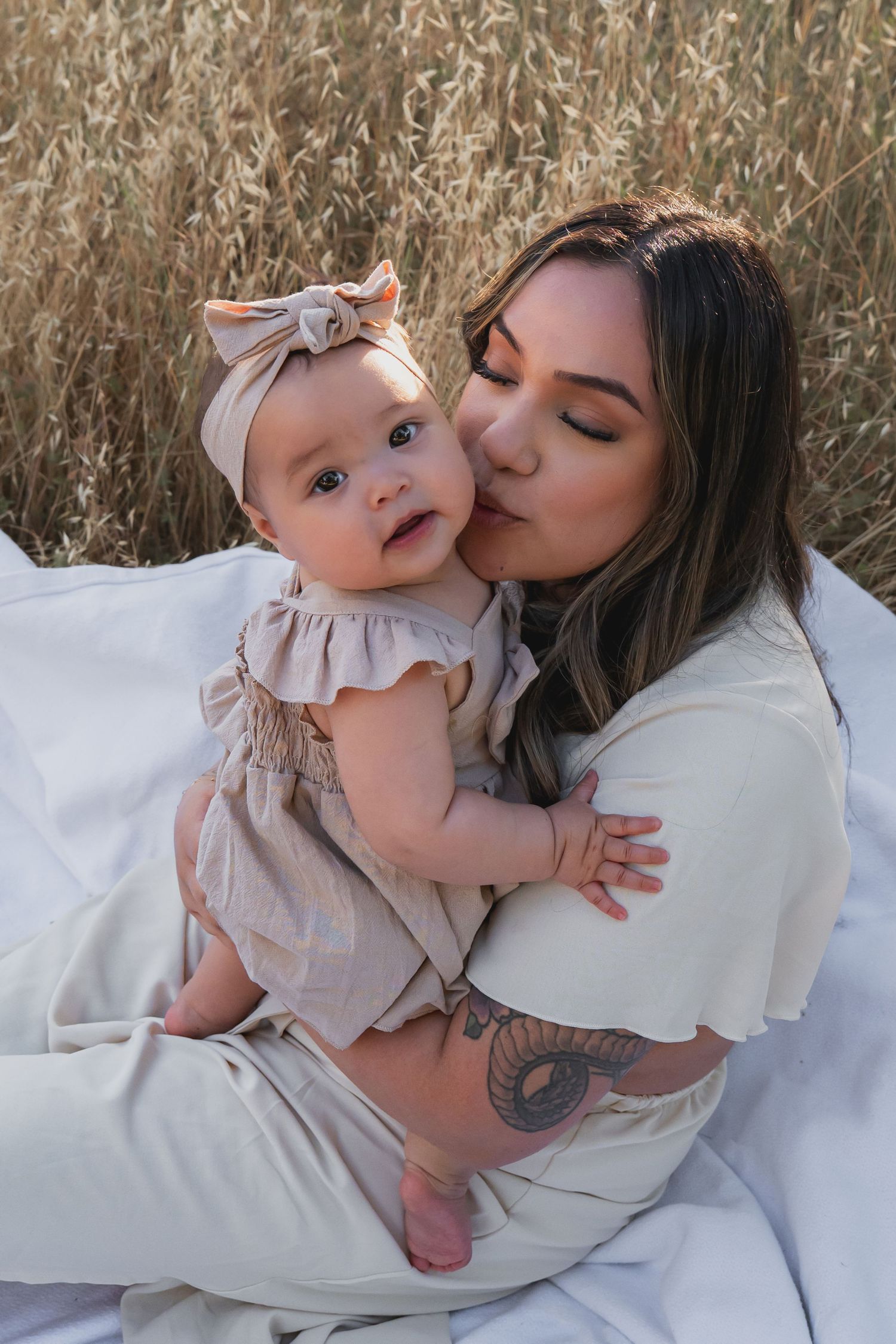 Tender moments between parent and baby on white blanket in sunlit field.