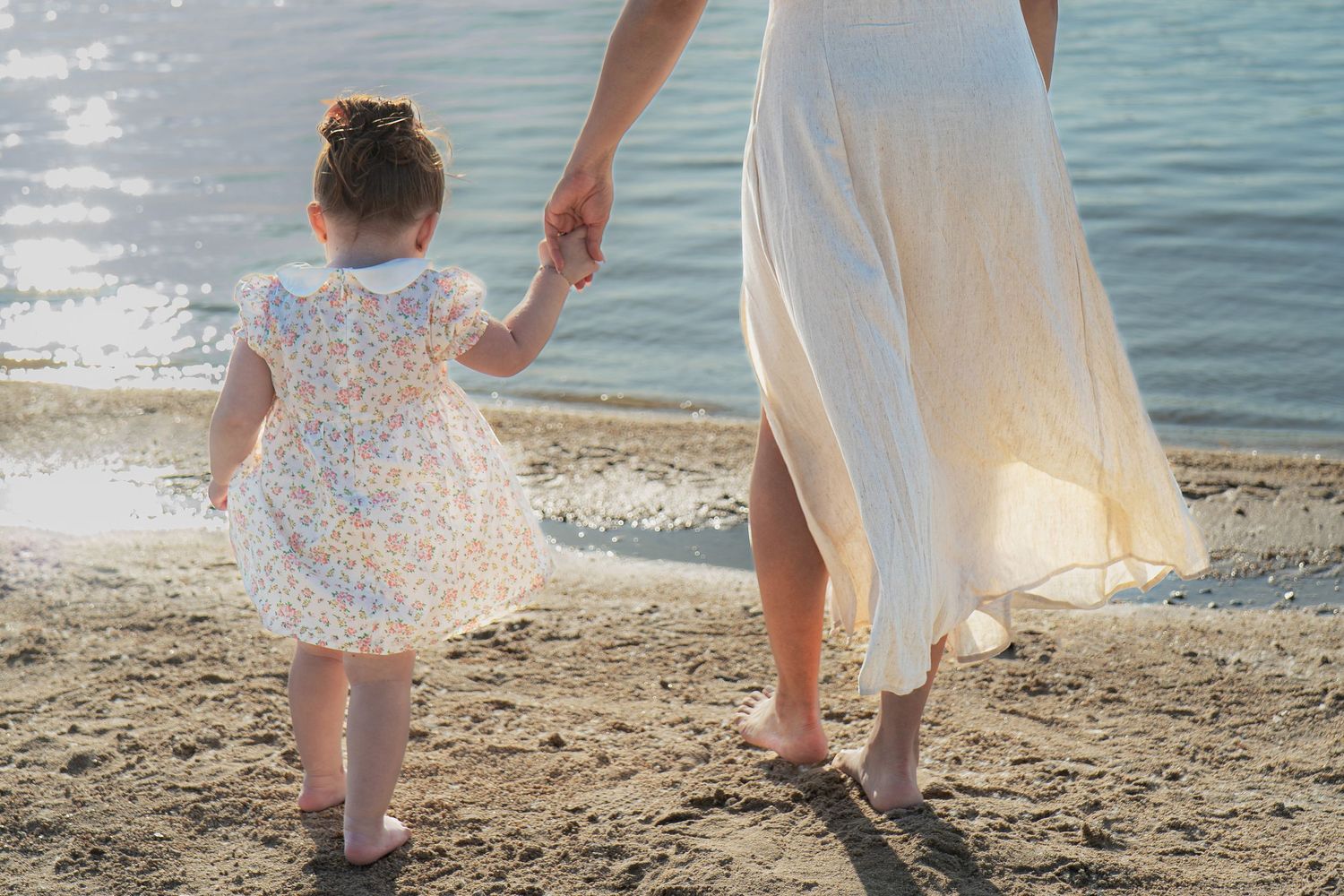 A family walks along the beach shoreline at sunset, leaving footprints in the sand.