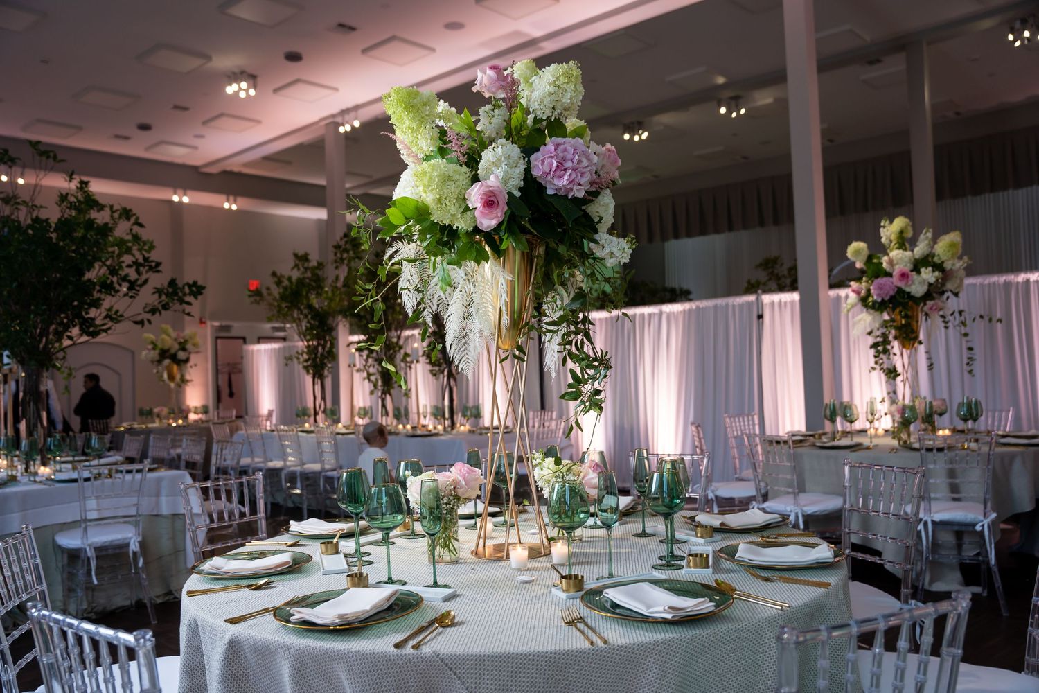 Elegant wedding reception hall with white tables, floral centerpieces, and soft pink lighting creating a romantic atmosphere.