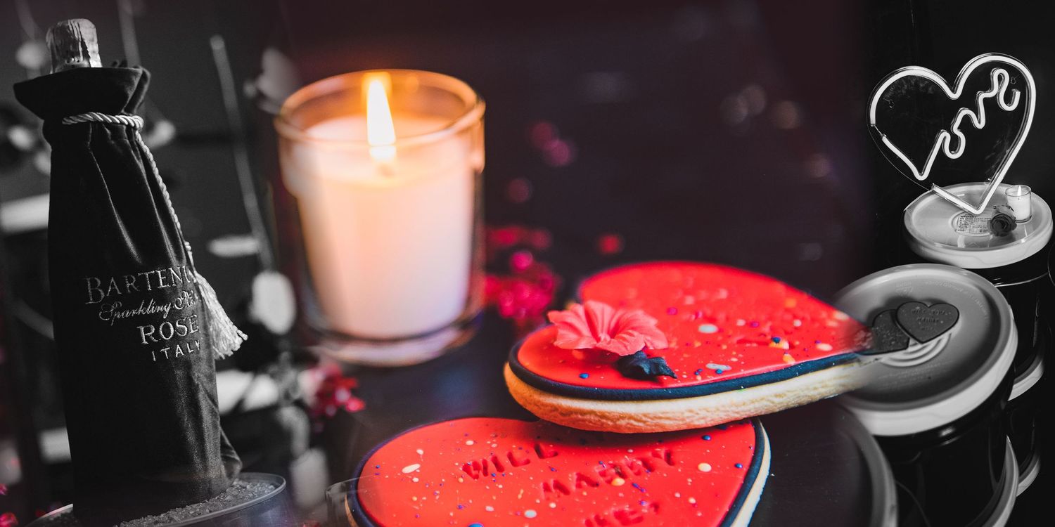 A glowing red candle creates a romantic ambiance in a dark setting with wine glasses visible in the background.
