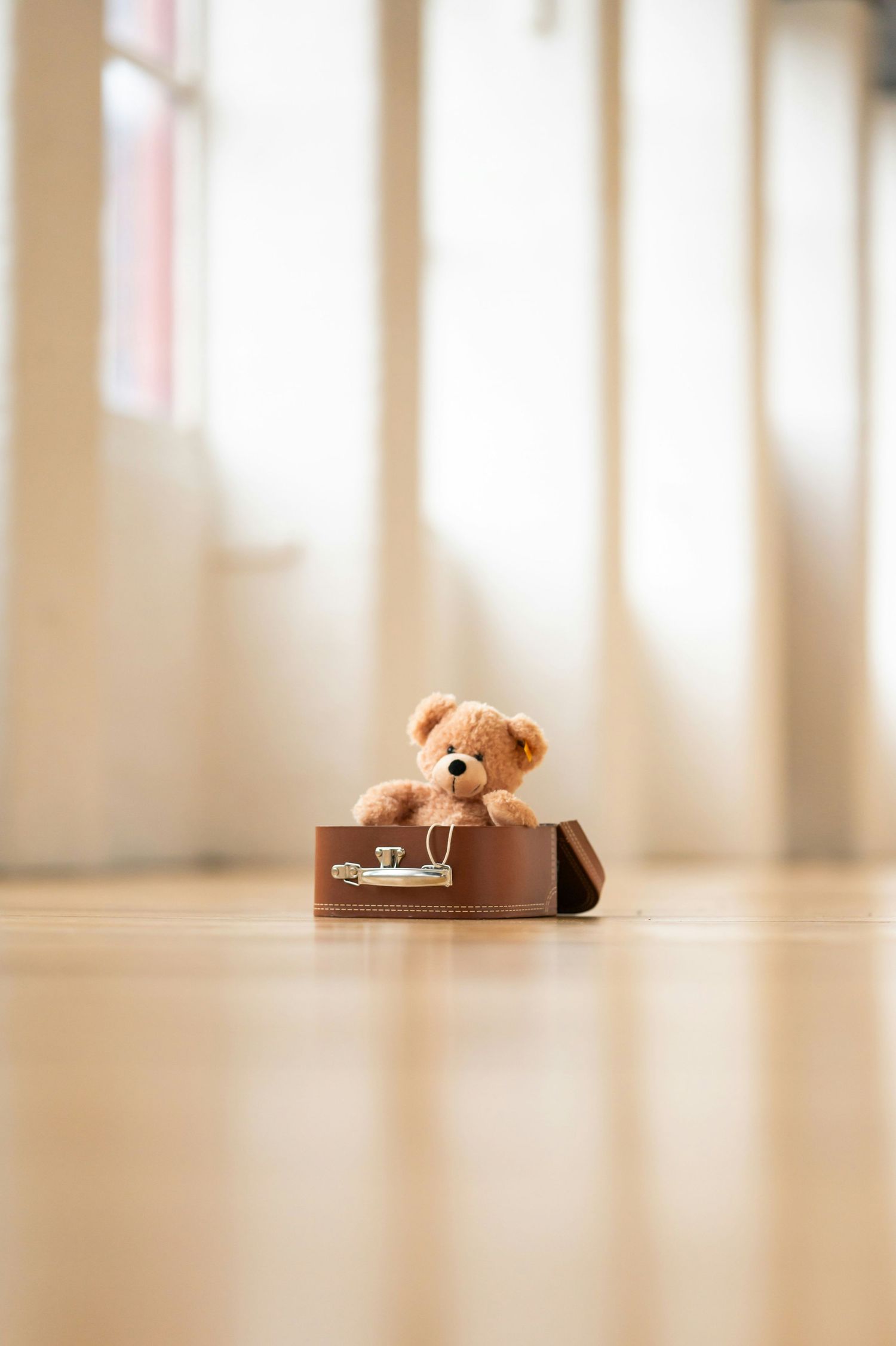 Cute teddy bear in a small suitcase, symbolizing comfort and new beginnings for baby and maternity albums.