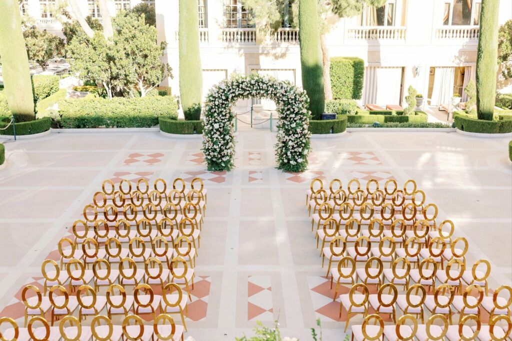 Elegant outdoor wedding ceremony setup with rows of wooden chairs and a floral arch at the end of the aisle.