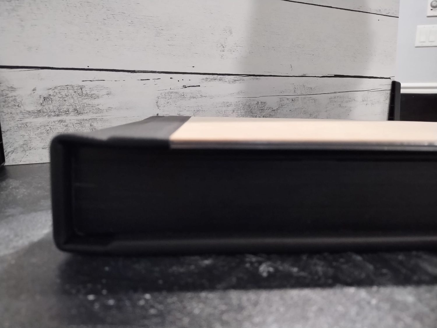 Side view of wood cover photo album with black page gilding displayed on a black marbled surface.
