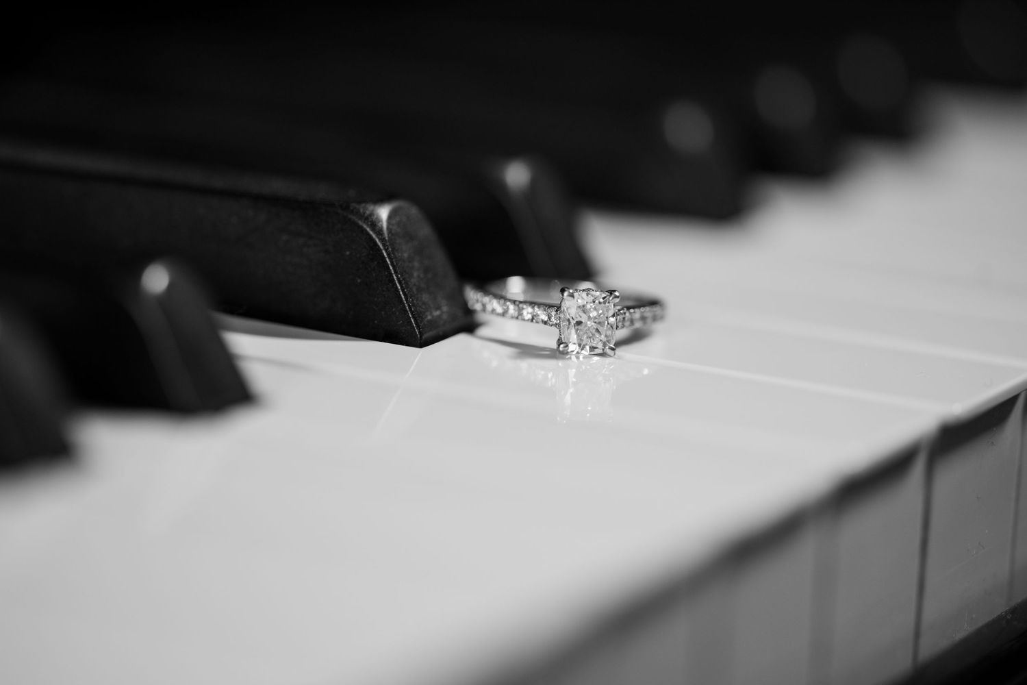 Black and white photo of a diamond engagement ring resting on piano keys.
