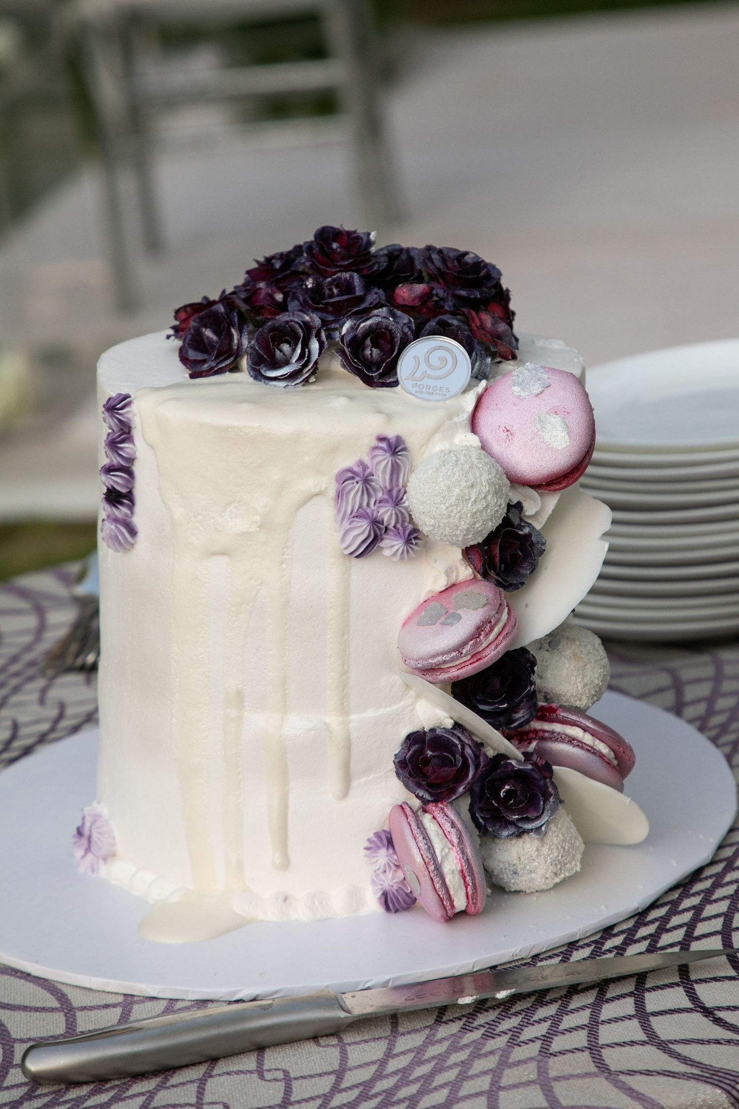 White wedding cake decorated with deep purple sugar roses and white sugar pearls displayed on a silver cake stand.