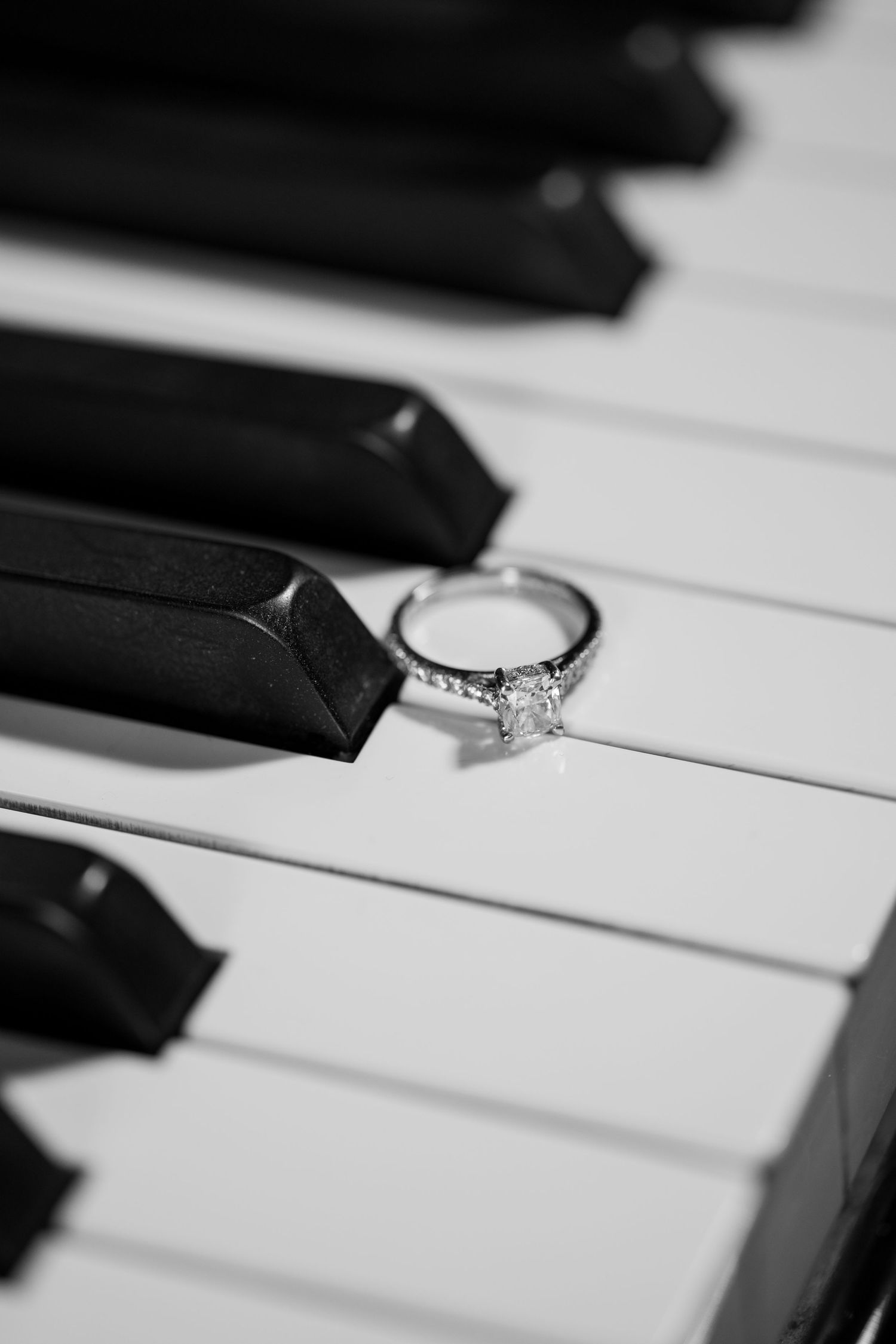 A sparkling diamond engagement ring sits elegantly on black and white piano keys in a romantic composition.