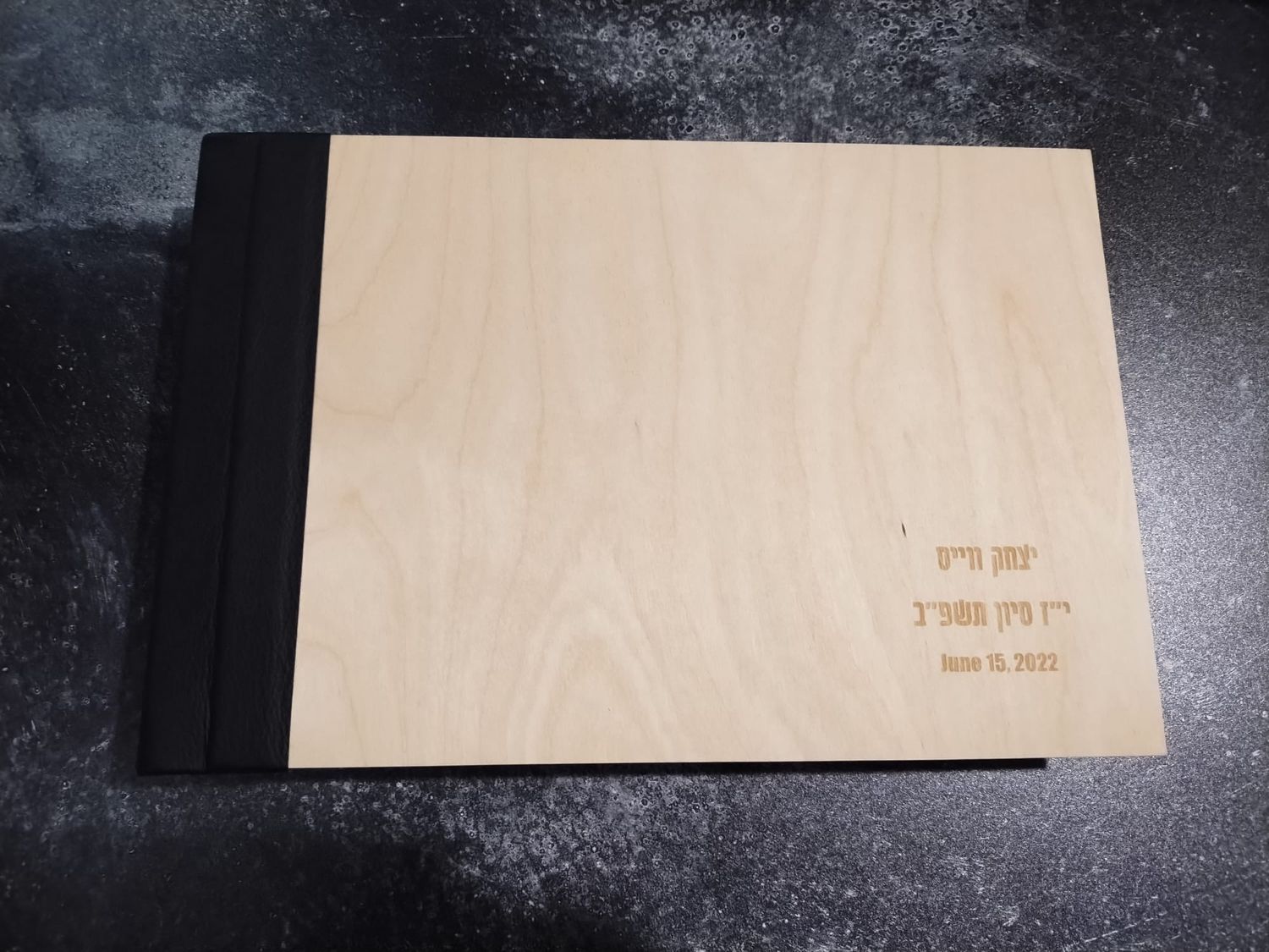 A minimalist wooden photo album or book cover with subtle engraved text on a dark surface.