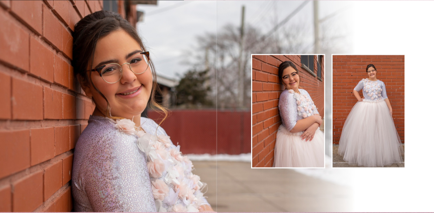 A bat mitzvah girl in a flowing tulle party dressdress poses against a rustic brick wall backdrop during a photoshoot.