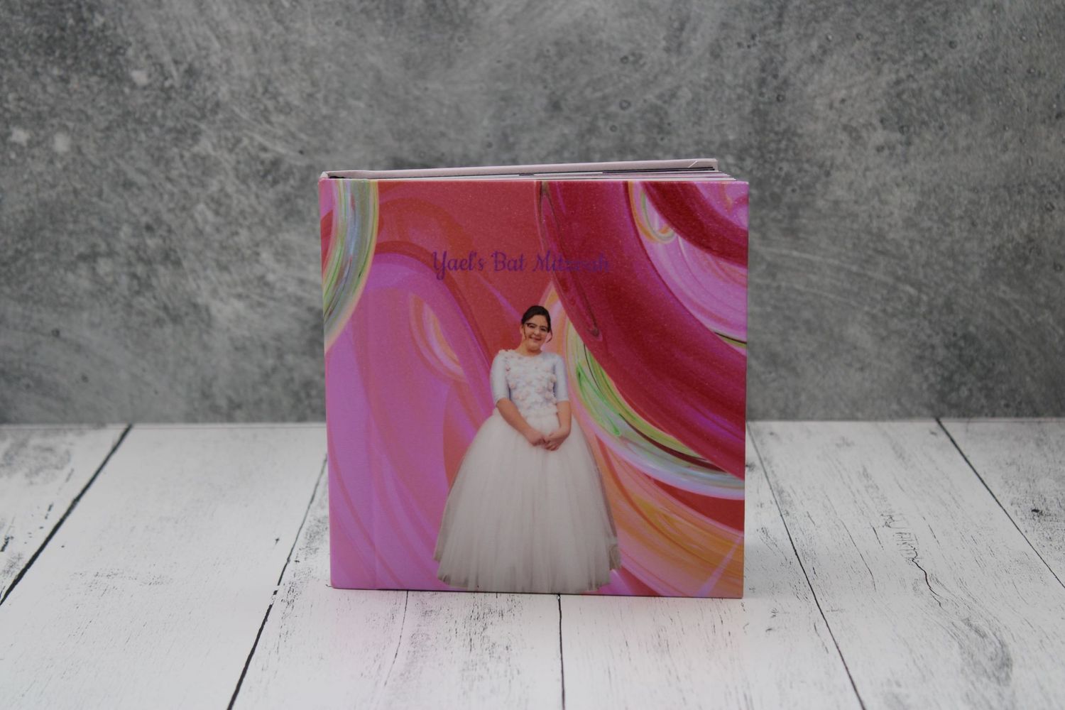 Pink photo book of a bat mitzvah girl displayed on a white wooden surface, symbolizing celebration and memory.