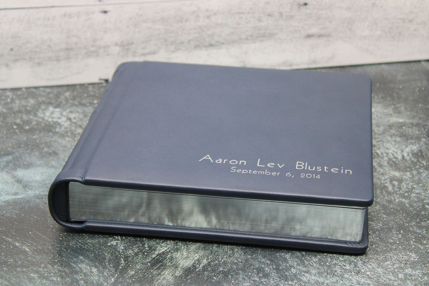 Cobalt blue leather photo album with silver page gilding displayed on a marbled surface.