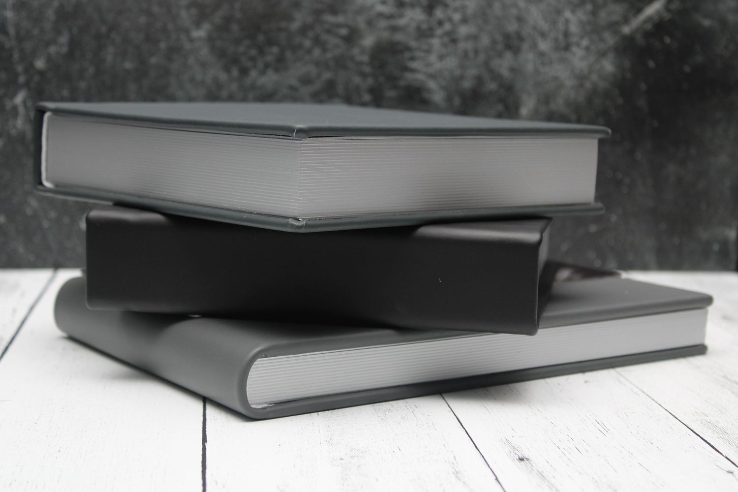 Charcoal gray photo albums arranged in a stack showing different angles and perspectives against a dark background.