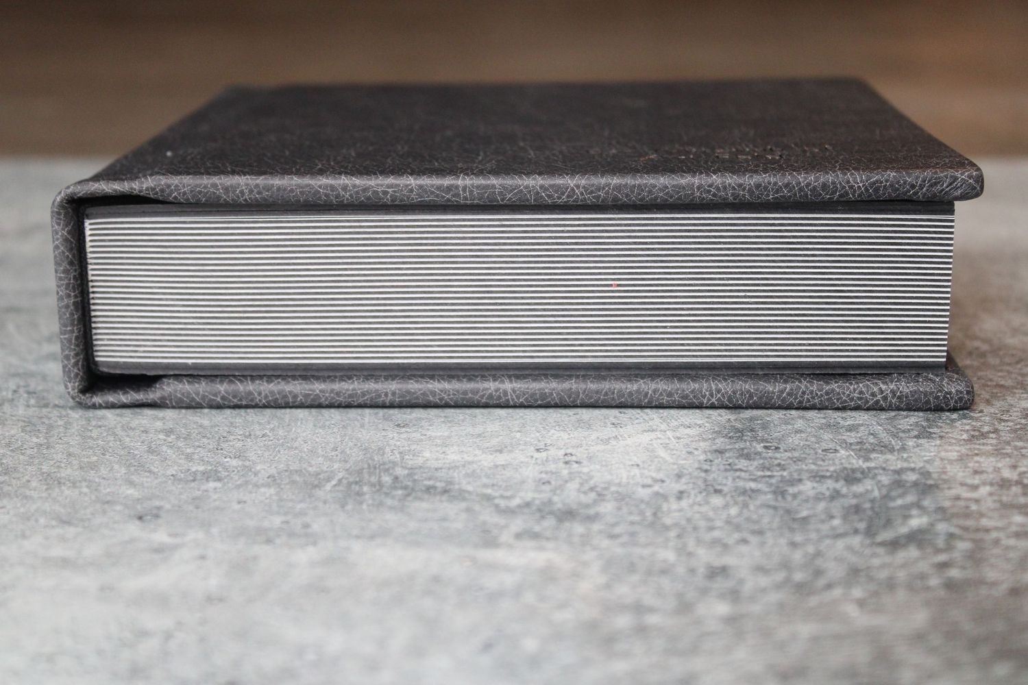 Side view of a closed gray hardcover photo album lying on a textured gray surface.