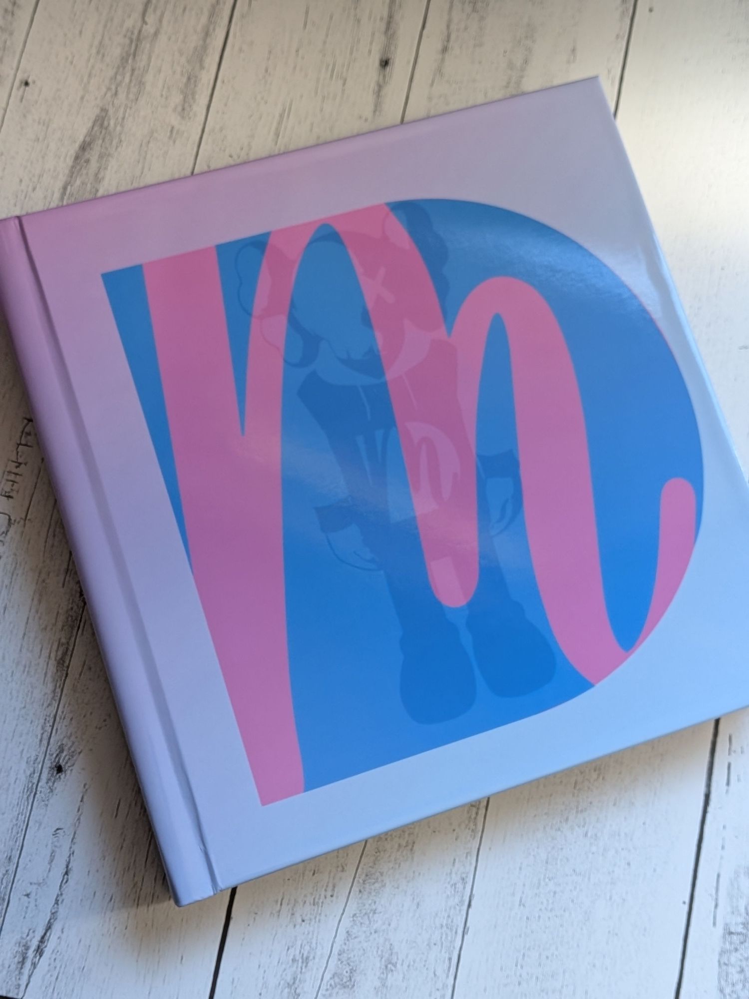 Pink and blue hardcover book with large decorative letter M on cover, displayed on white wood surface.