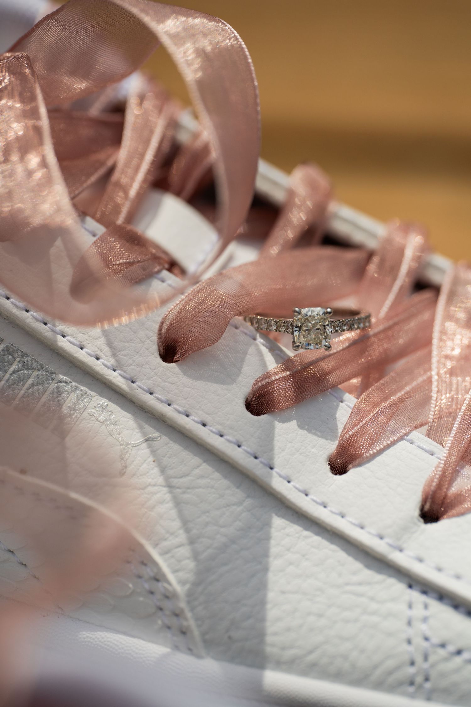 Close-up view of white leather sneaker with metallic rose gold laces showing detailed stitching pattern.