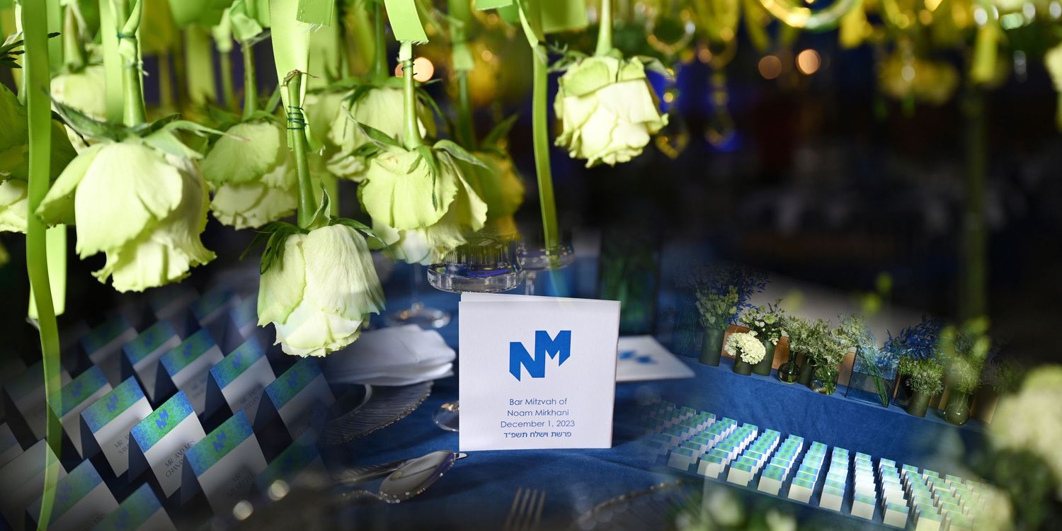 White carnation flowers hanging above a business card and blue reflective surface in an elegant bar mitzvah event setting.