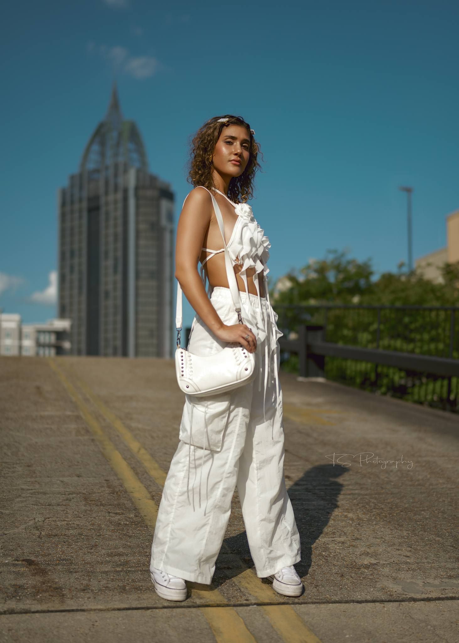 Urban fashion shot with white outfit against city skyline featuring tall building.