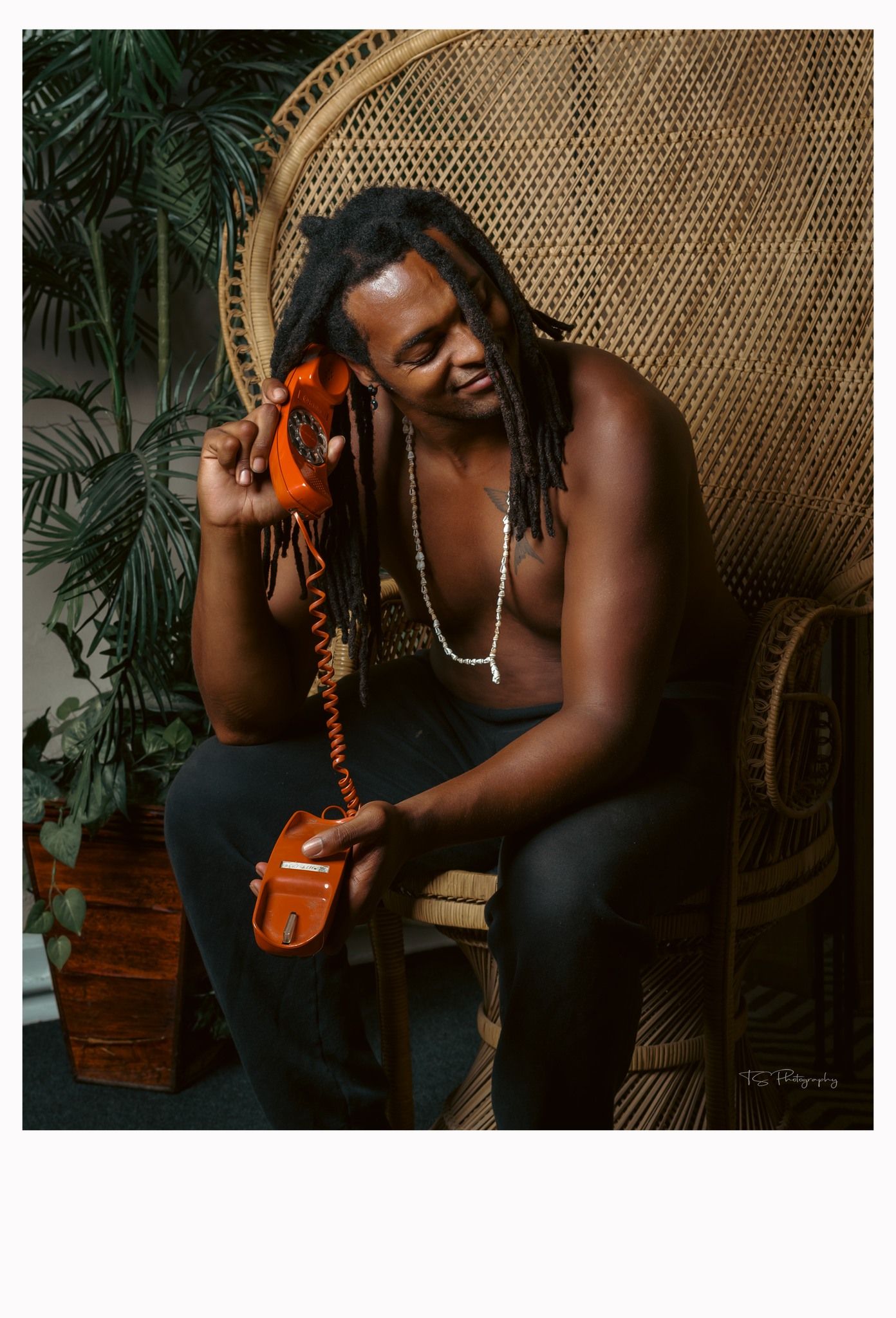 Artistic portrait in wicker peacock chair with plants and vintage telephone.