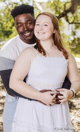 A happy couple embracing outdoors in casual white clothing on a sunny day.