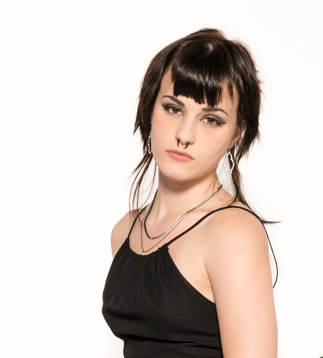 Studio portrait against white backdrop featuring dark bangs, black tank top and silver necklace.