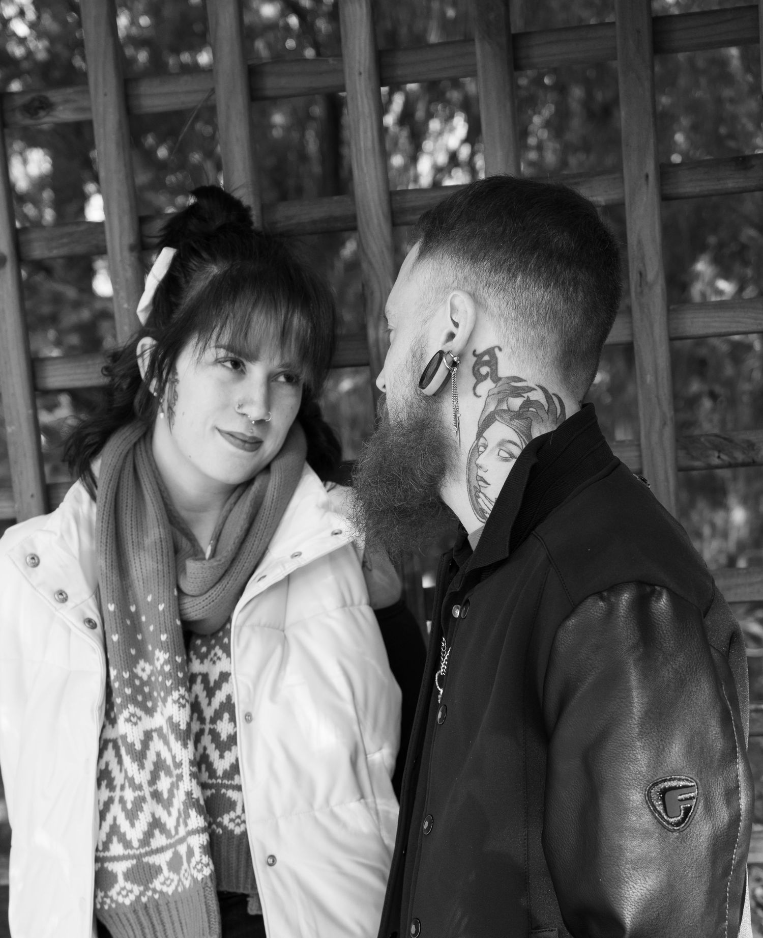 Couple in winter clothing pose together in front of latticed window structure.