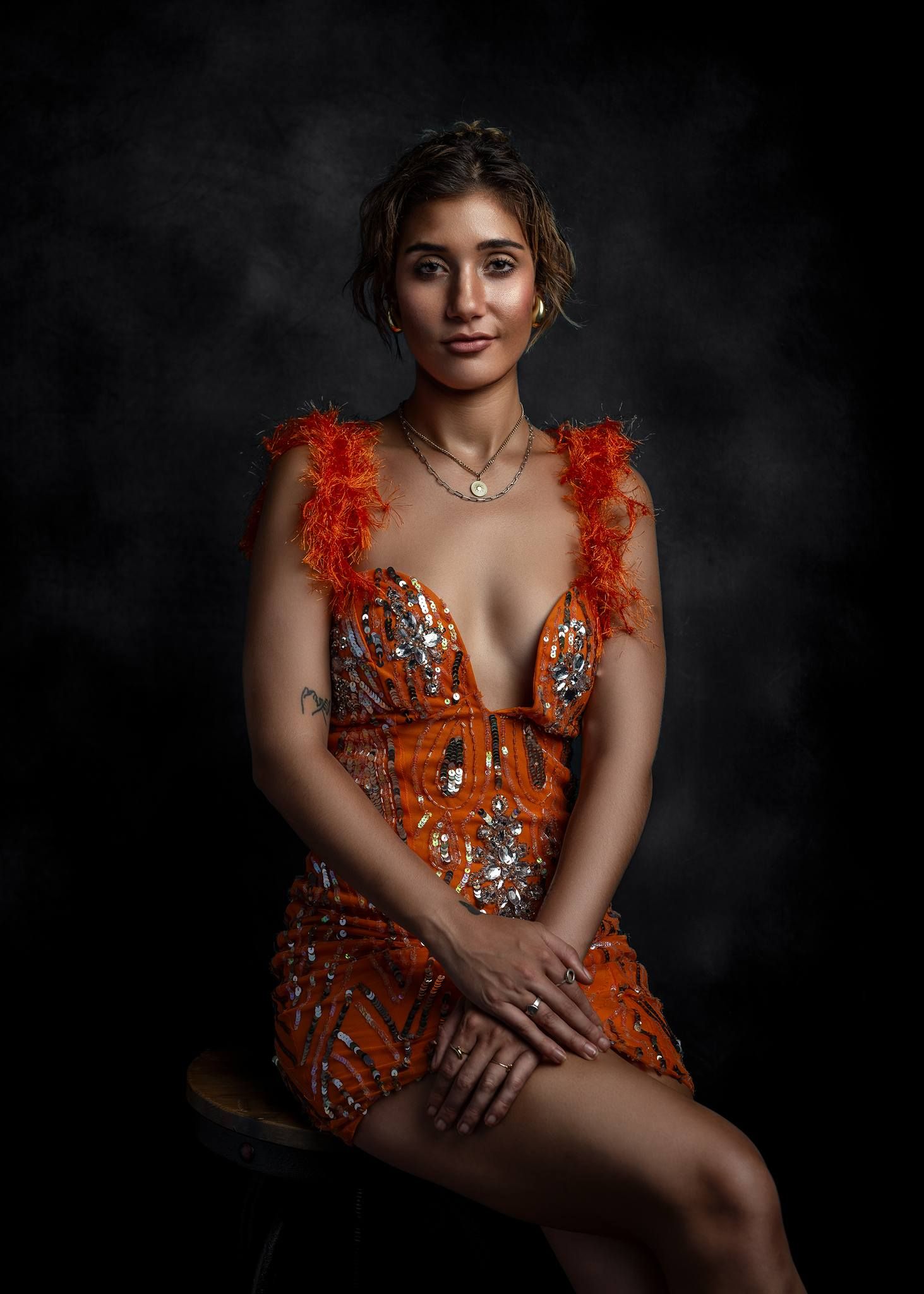 Glamour portrait in orange sequined dress against dark background.
