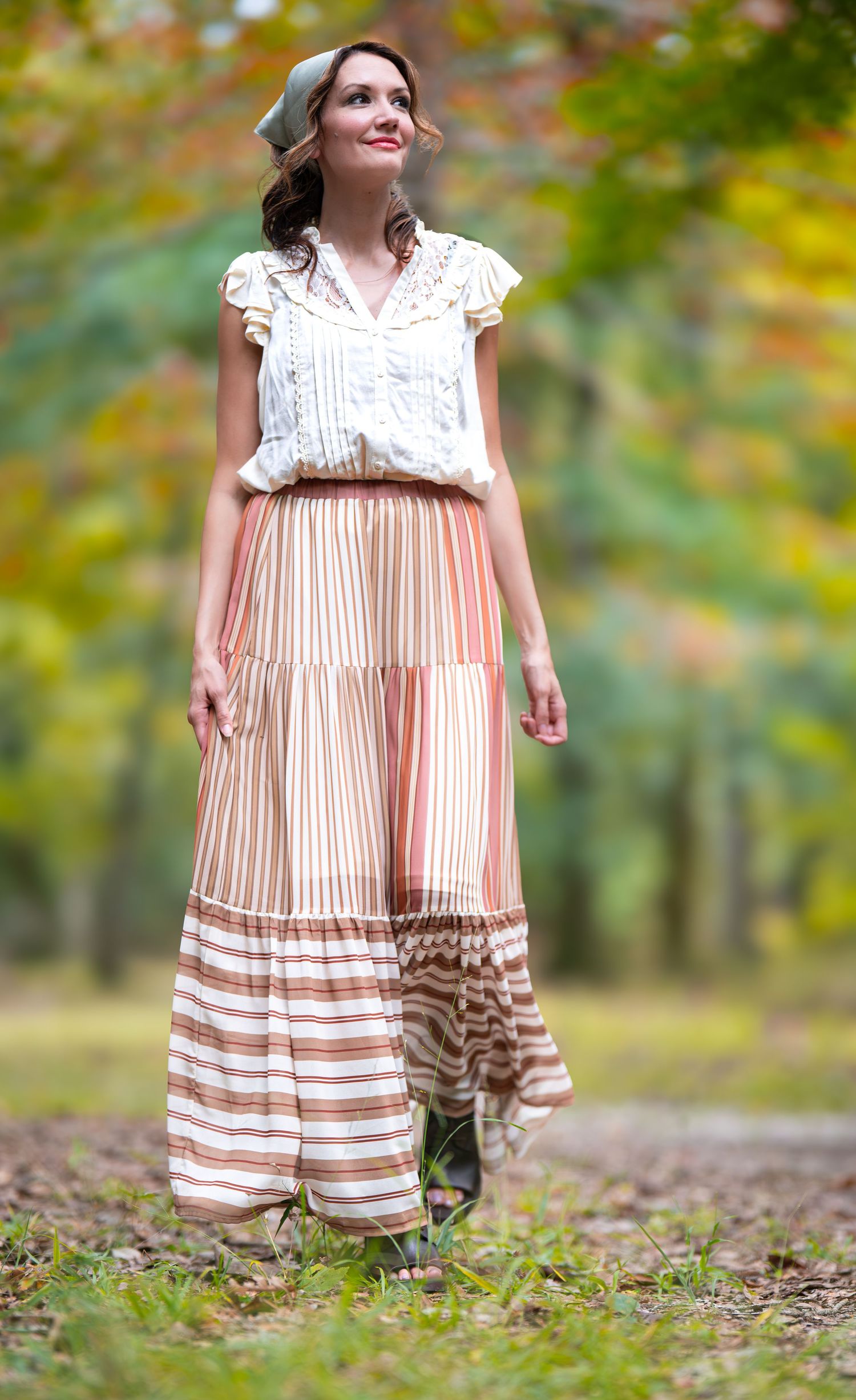 Woman in vintage-inspired outfit with lace top and pleated maxi skirt posing in autumn setting.