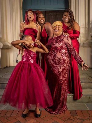 A group wearing elegant red formal dresses posing playfully together on a brick porch.