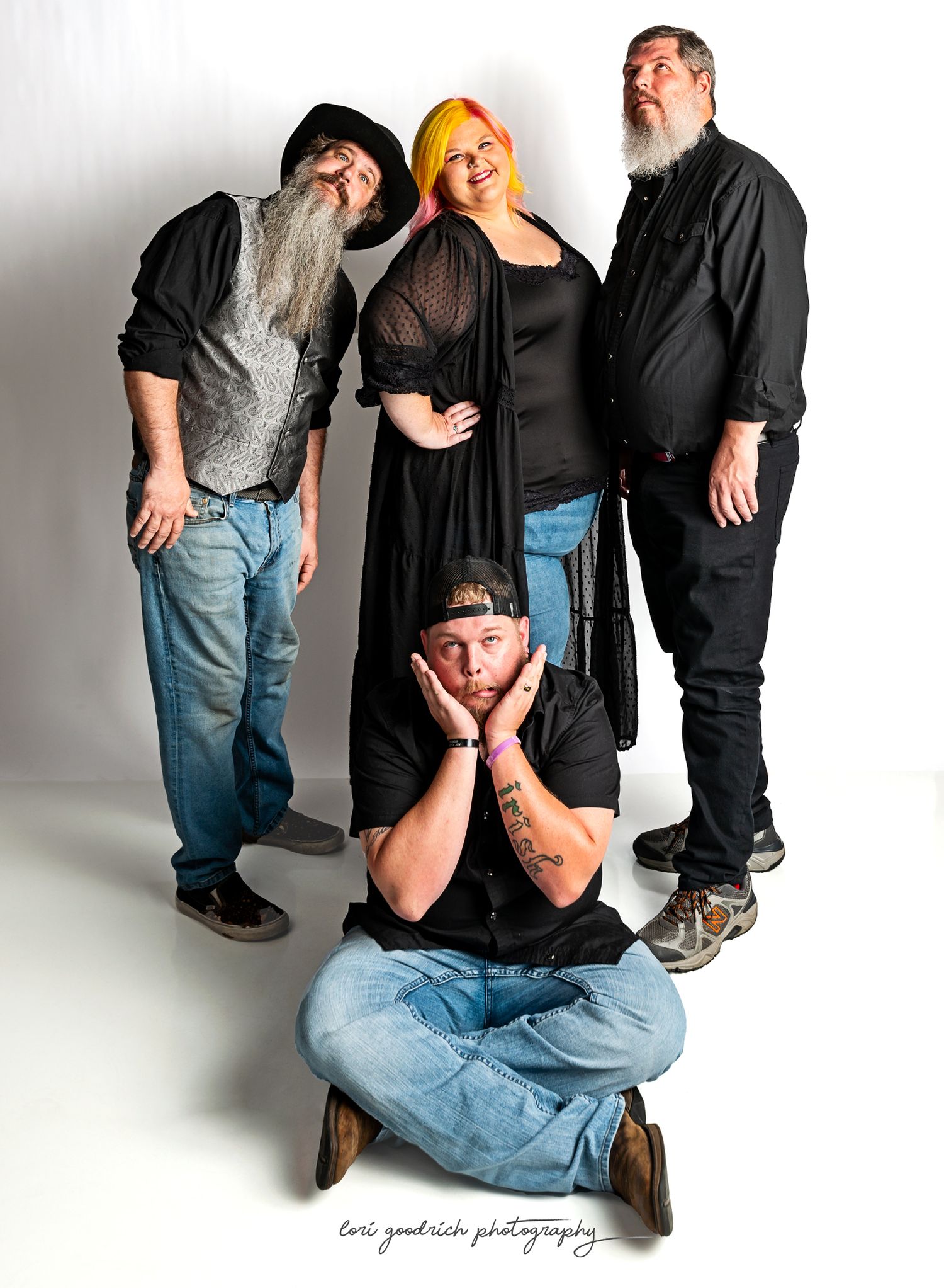 A group of four people pose together in a studio setting, with one sitting cross-legged on the floor.