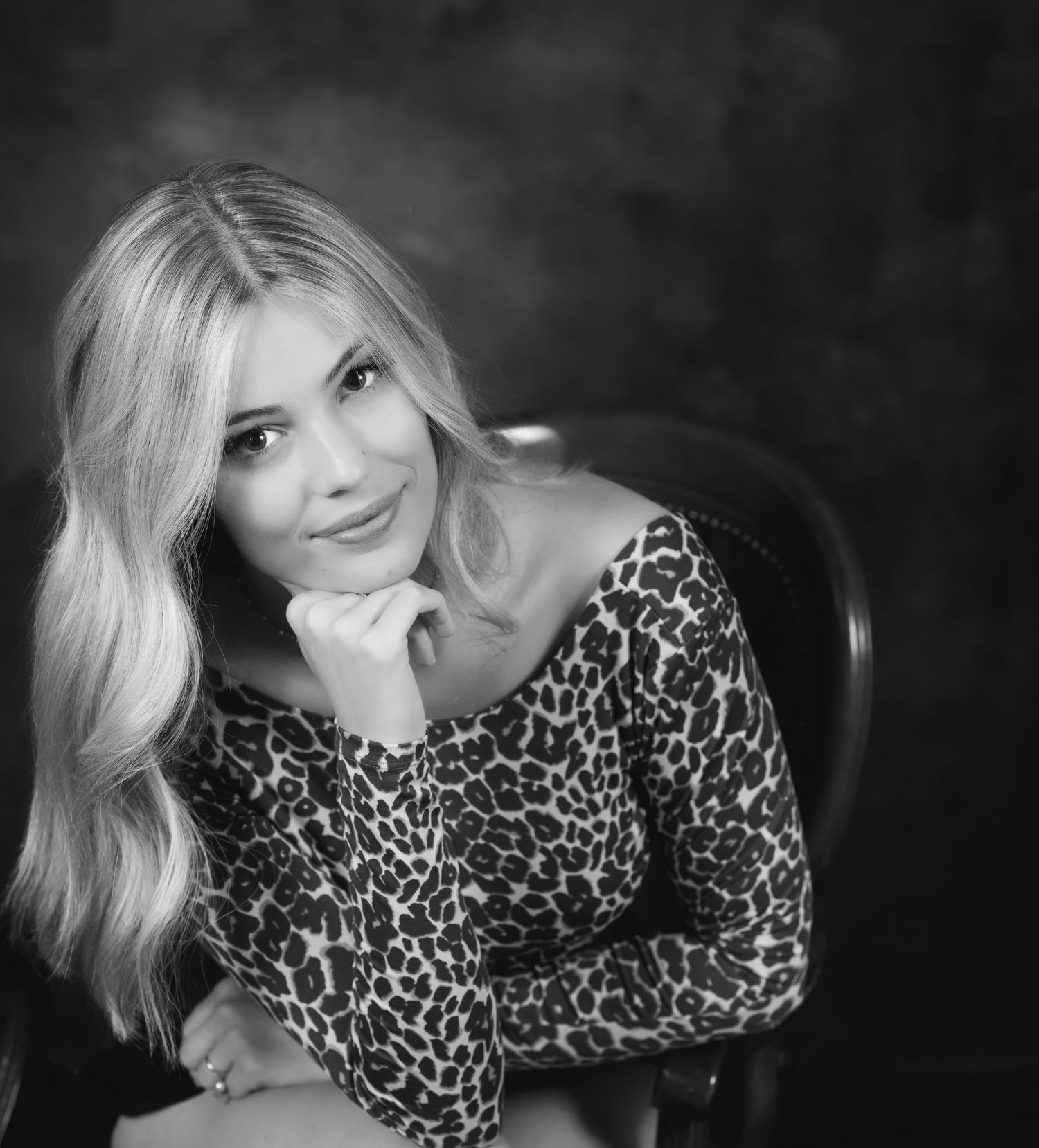 Black and white portrait of person in leopard print top posing with hand under chin.