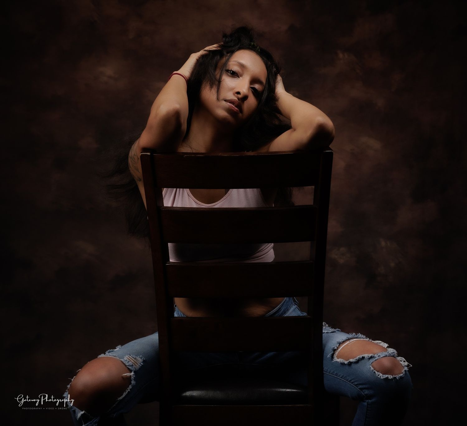 Moody portrait of someone posed dramatically on wooden chair.