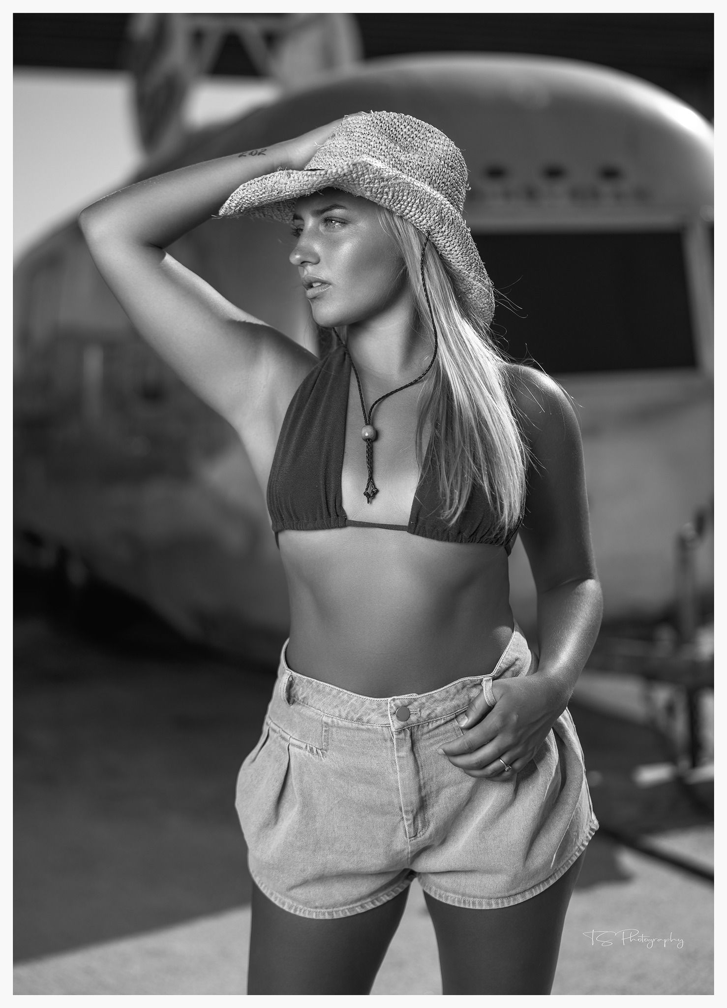 Black and white summer portrait with straw hat and denim shorts near vintage aircraft.
