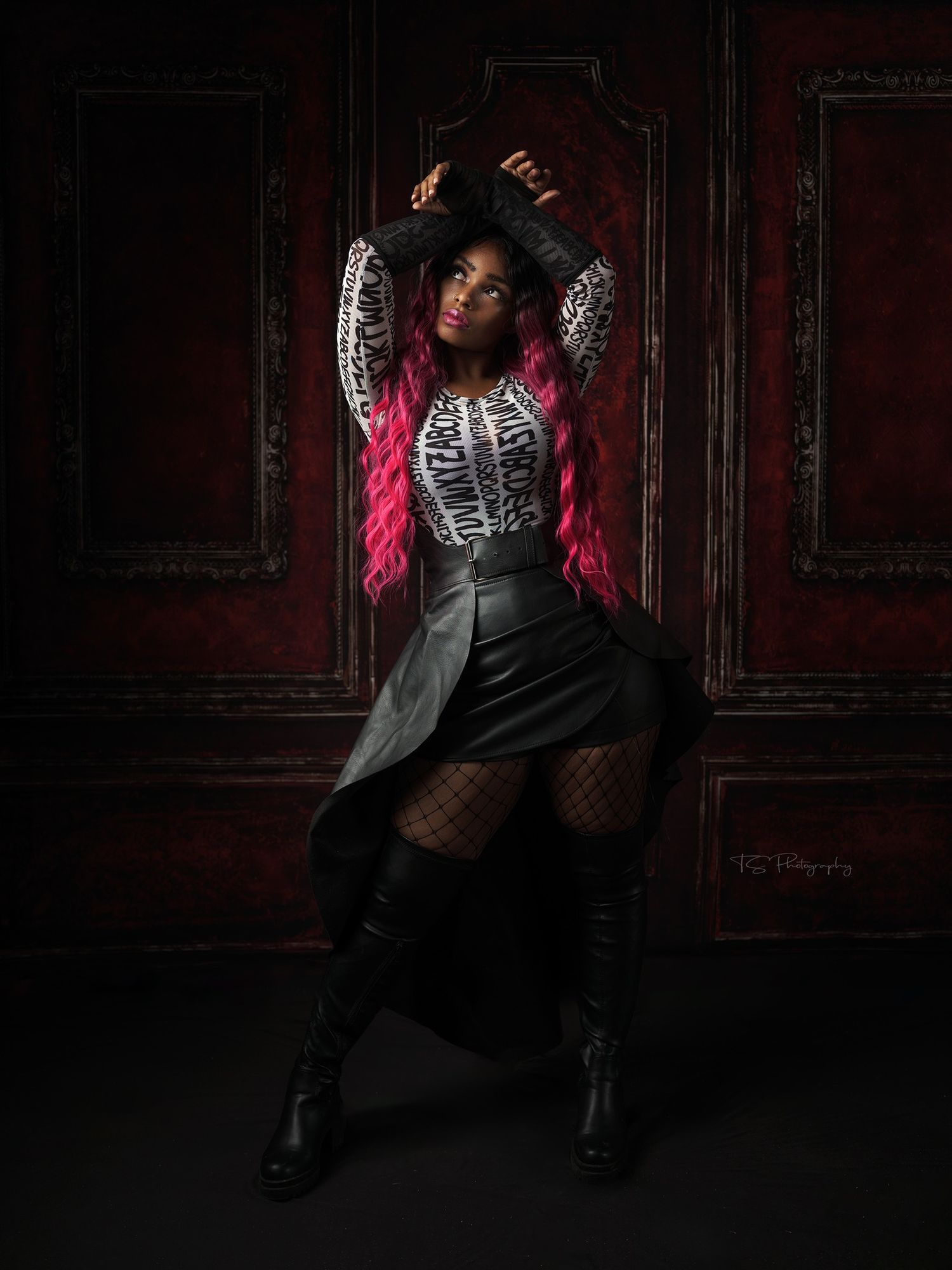 Dramatic fashion portrait with pink and silver outfit against dark red paneled wall.