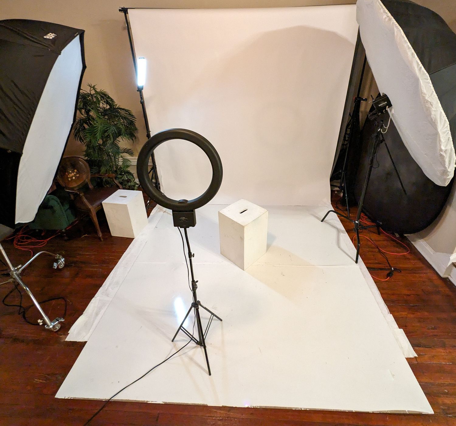 Photography studio setup with ring light, white backdrop, and softbox lighting equipment arranged on wooden floor.