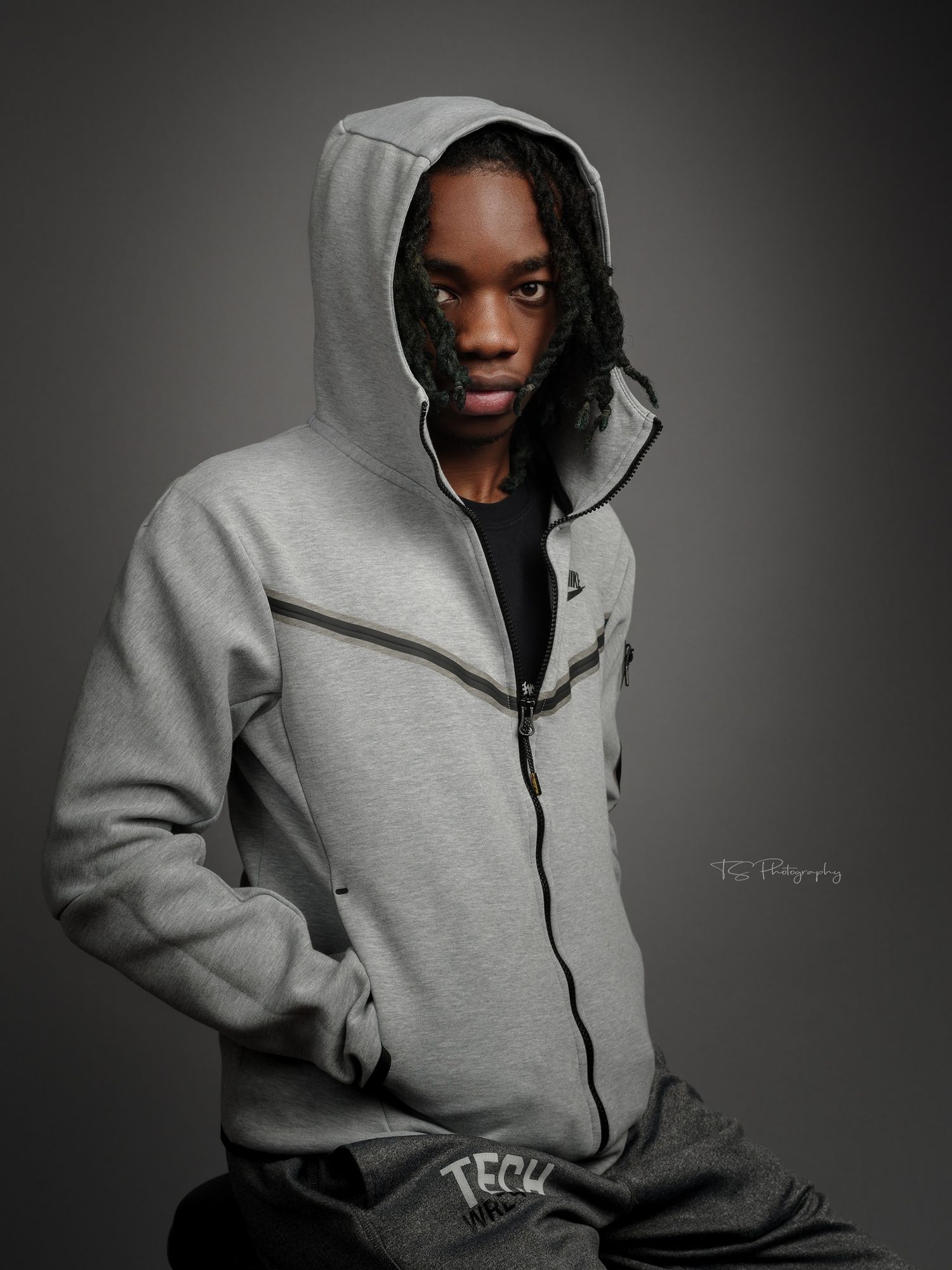 Portrait in grey hoodie against dark background with dramatic lighting.