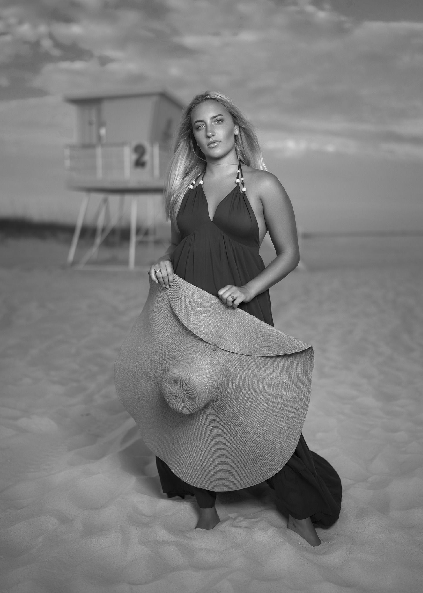 A black and white beach portrait featuring a long black dress and lifeguard tower in the background.